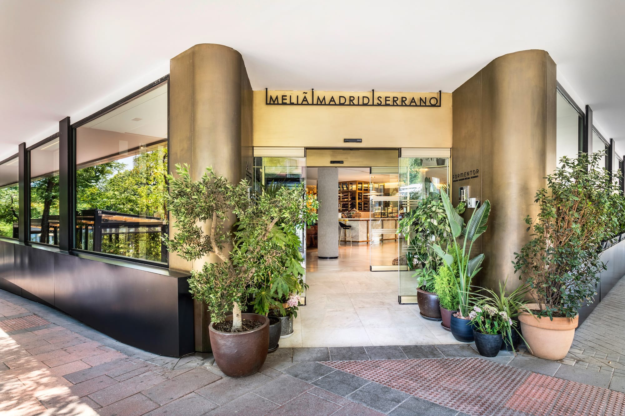 Meliá Madrid Serrano hotel entrance, modern glass facade and potted plants.