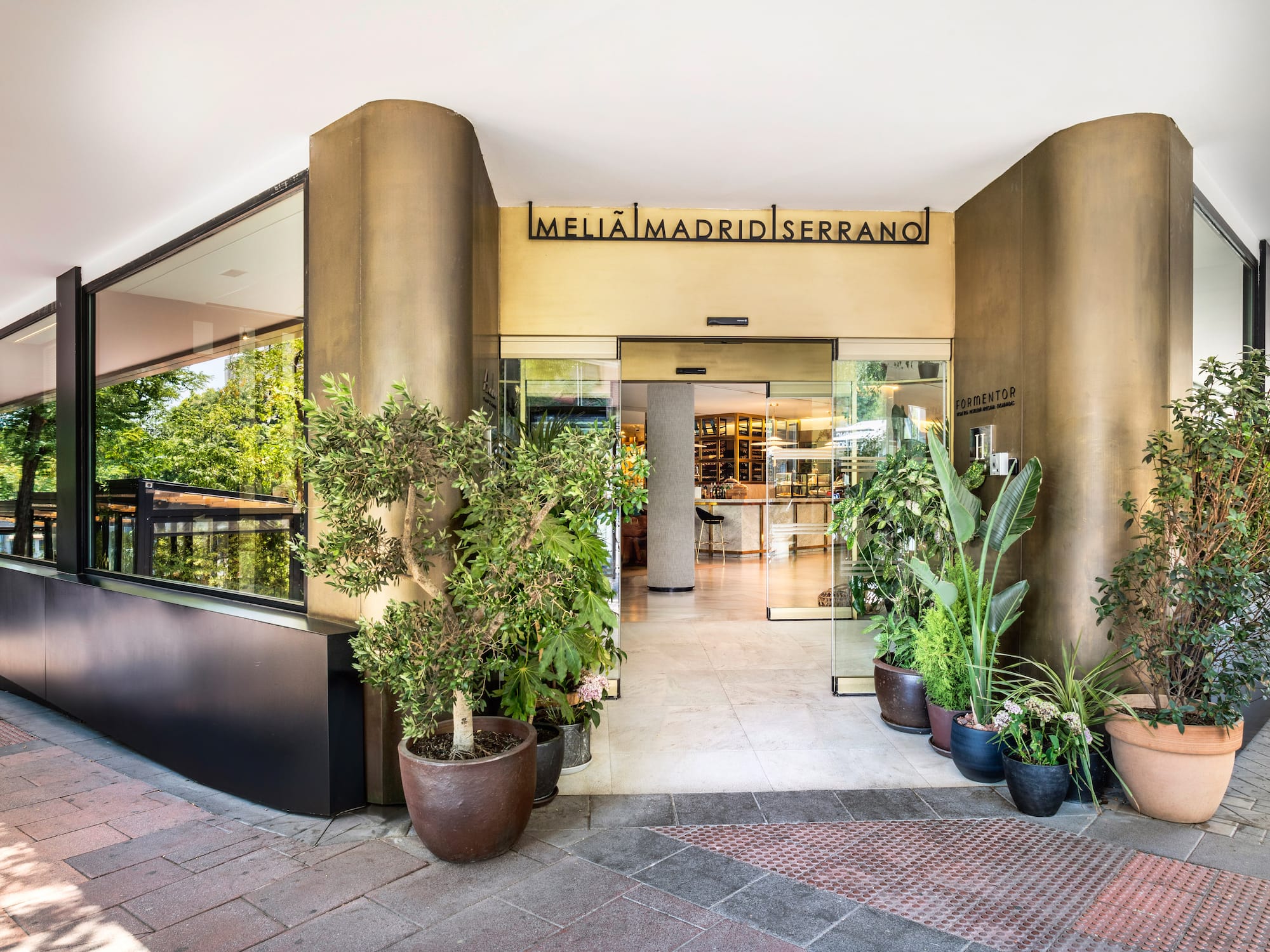 Meliã Madrid Serrano hotel entrance with glass doors, modern facade, and potted plants.