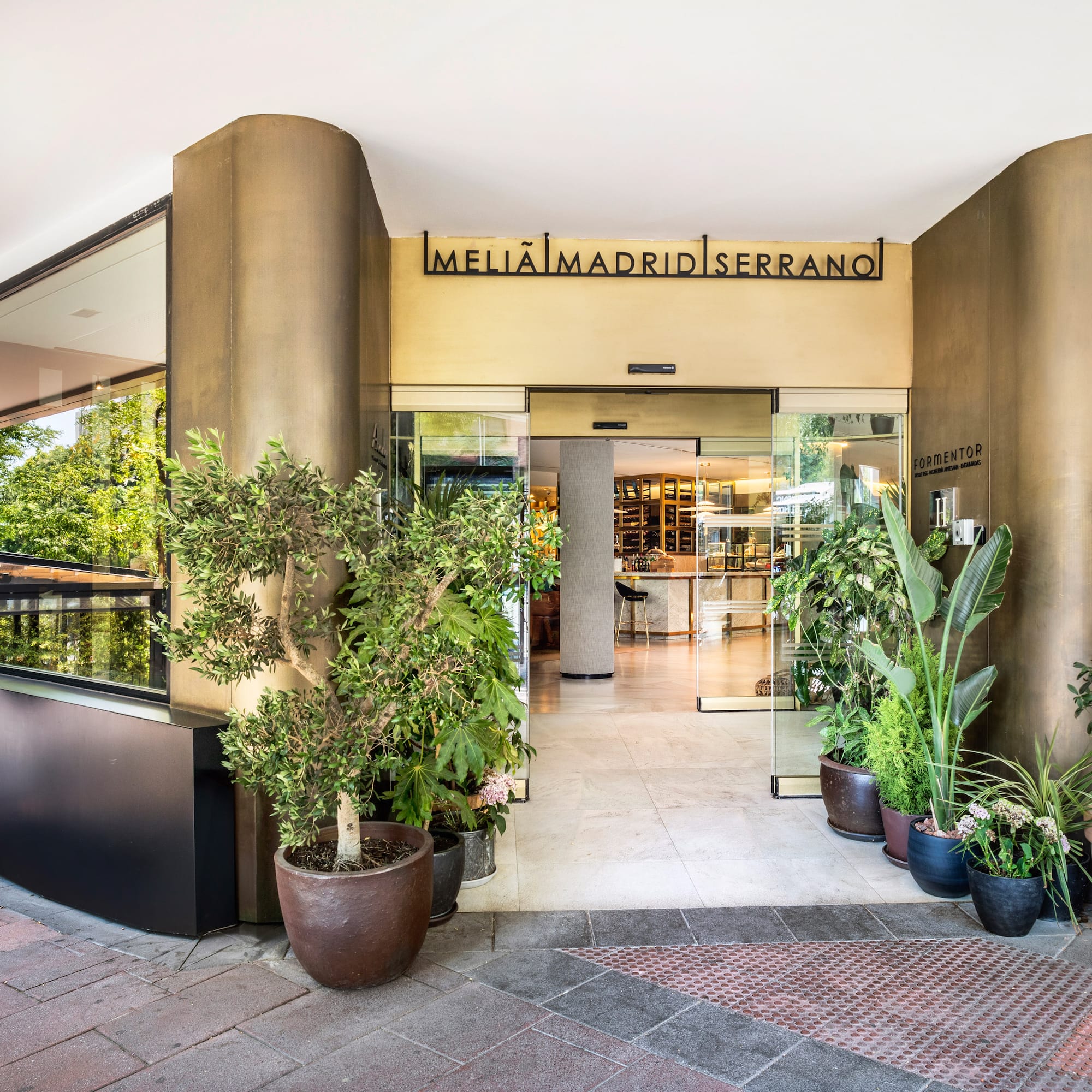 Meliã Madrid Serrano hotel entrance with glass doors, modern facade, and potted plants.