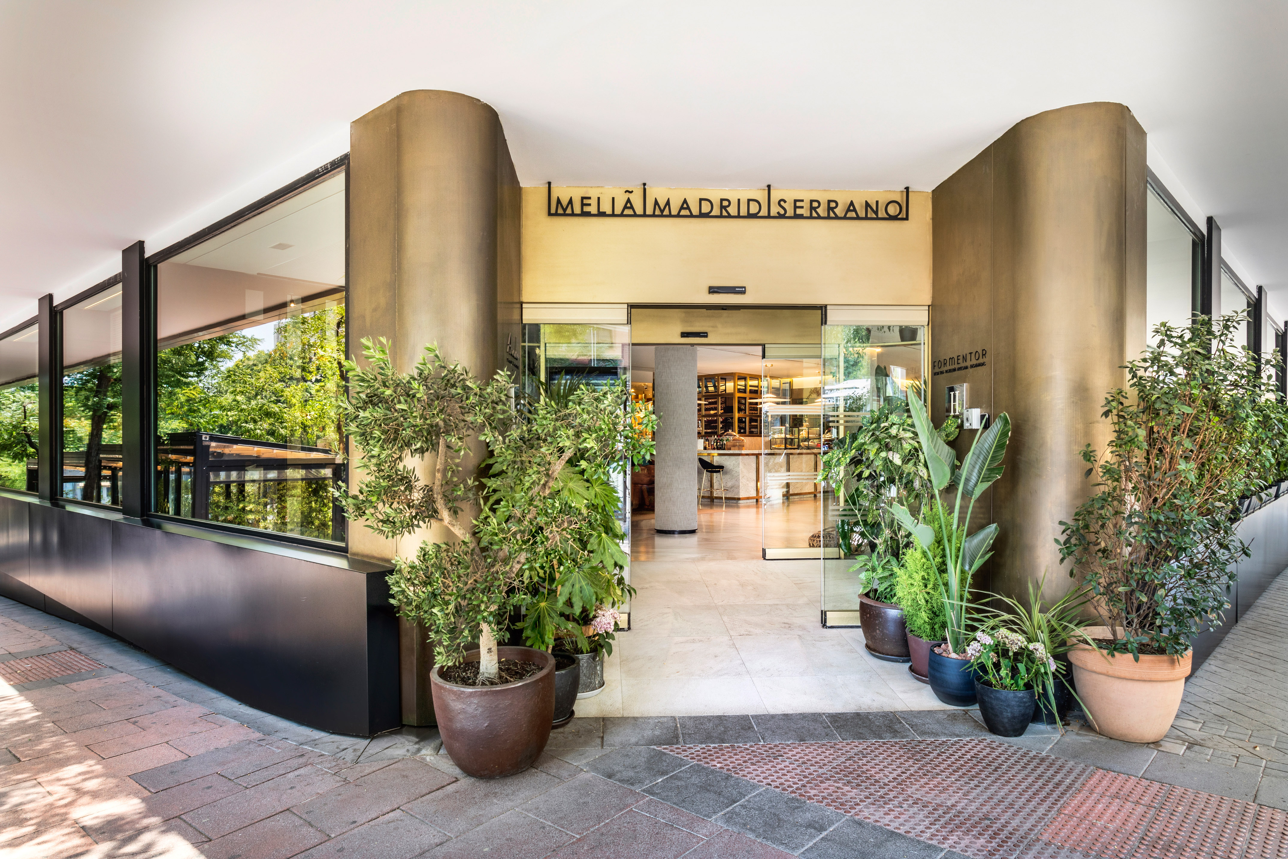 Meliã Madrid Serrano hotel entrance with glass doors, modern facade, and potted plants.