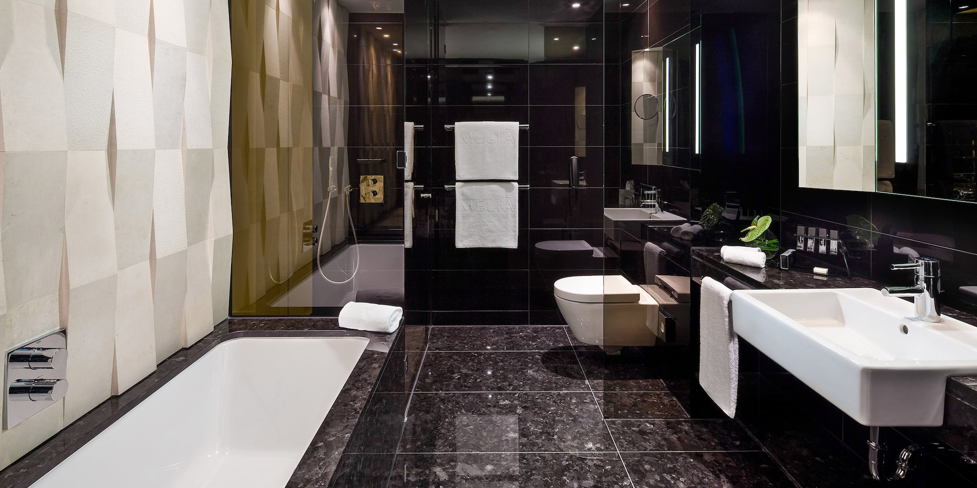 Modern black luxury bathroom with white tub, sink, and textured accent wall.