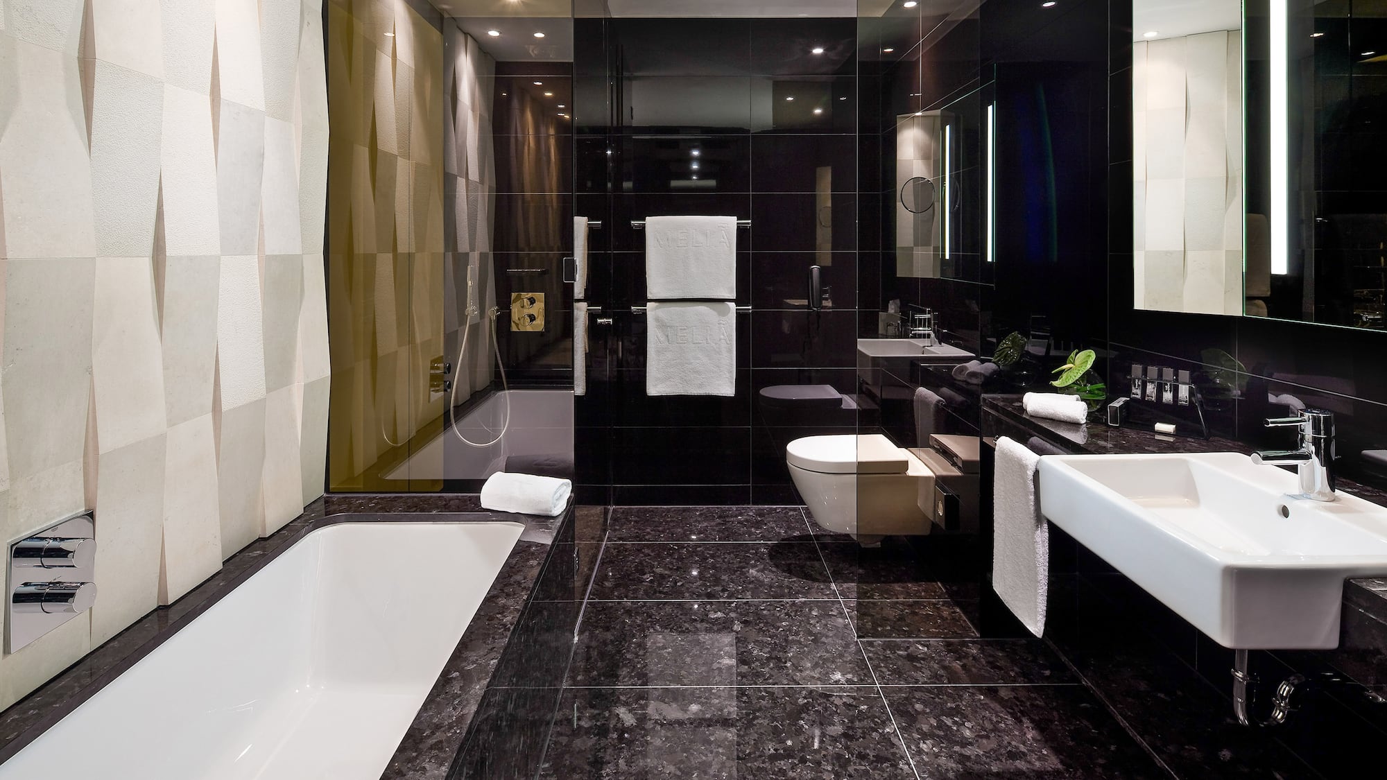 Modern black luxury bathroom with white tub, sink, and textured accent wall.