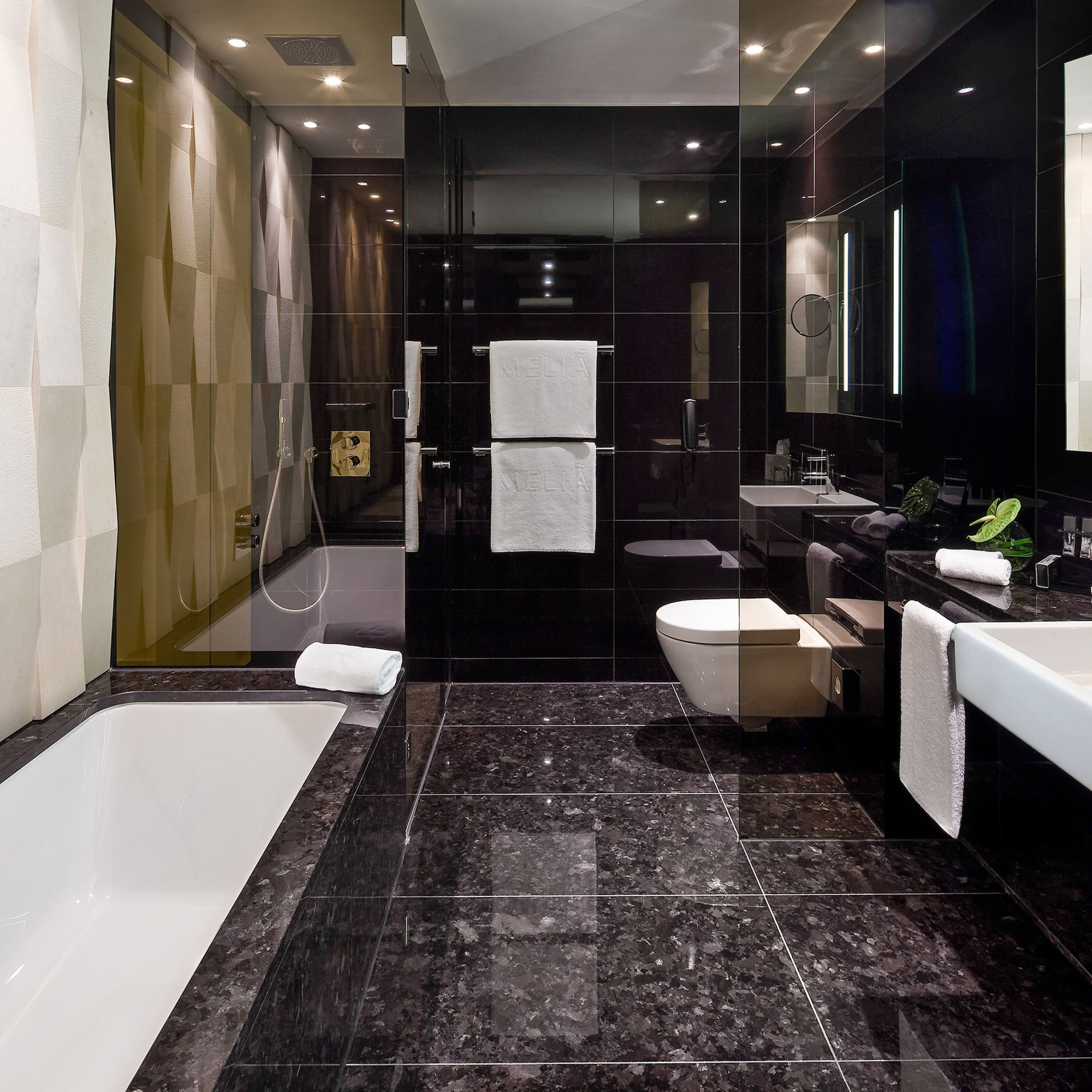 Modern hotel bathroom with black granite, white fixtures, sleek design, textured wall.