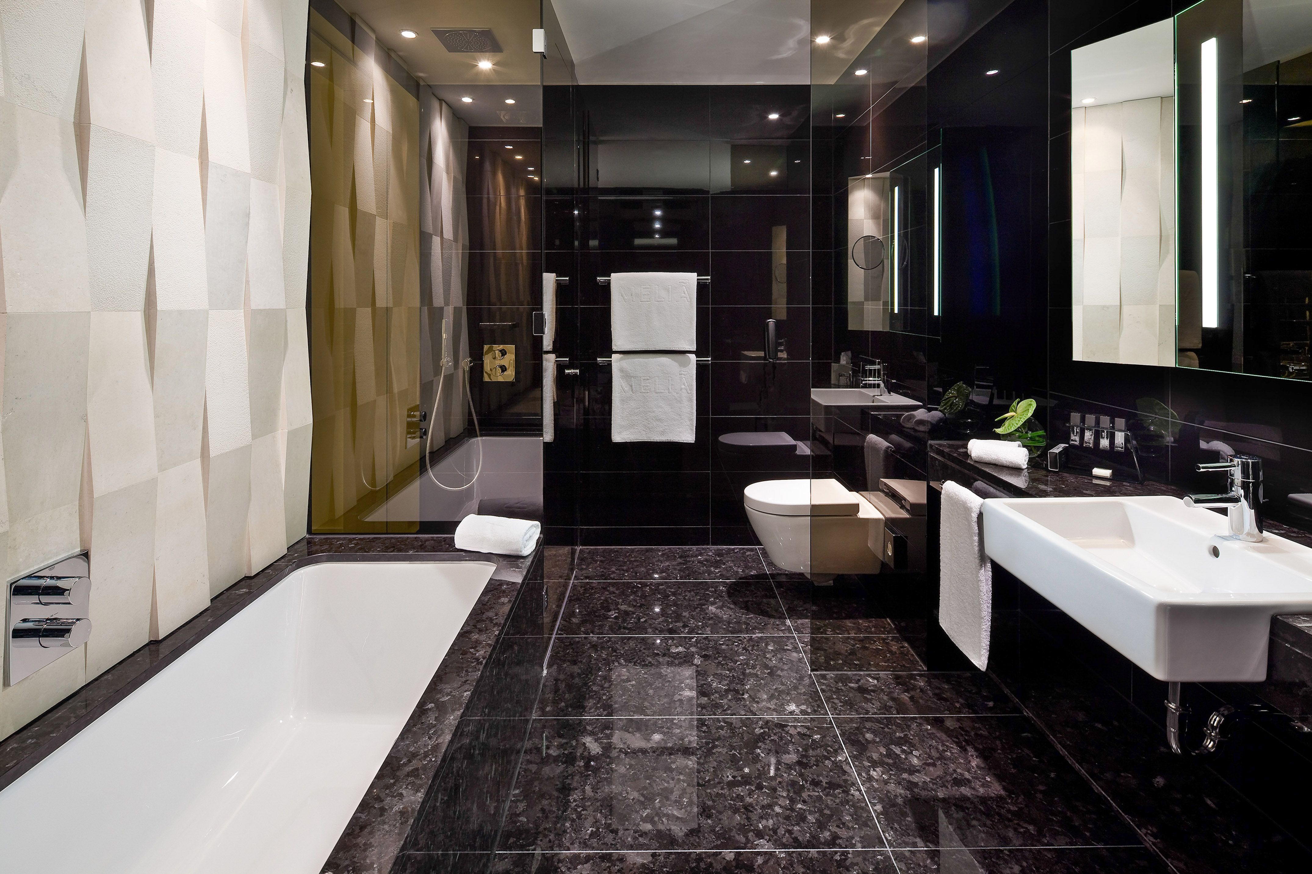 Modern black luxury bathroom with white tub, sink, and textured accent wall.