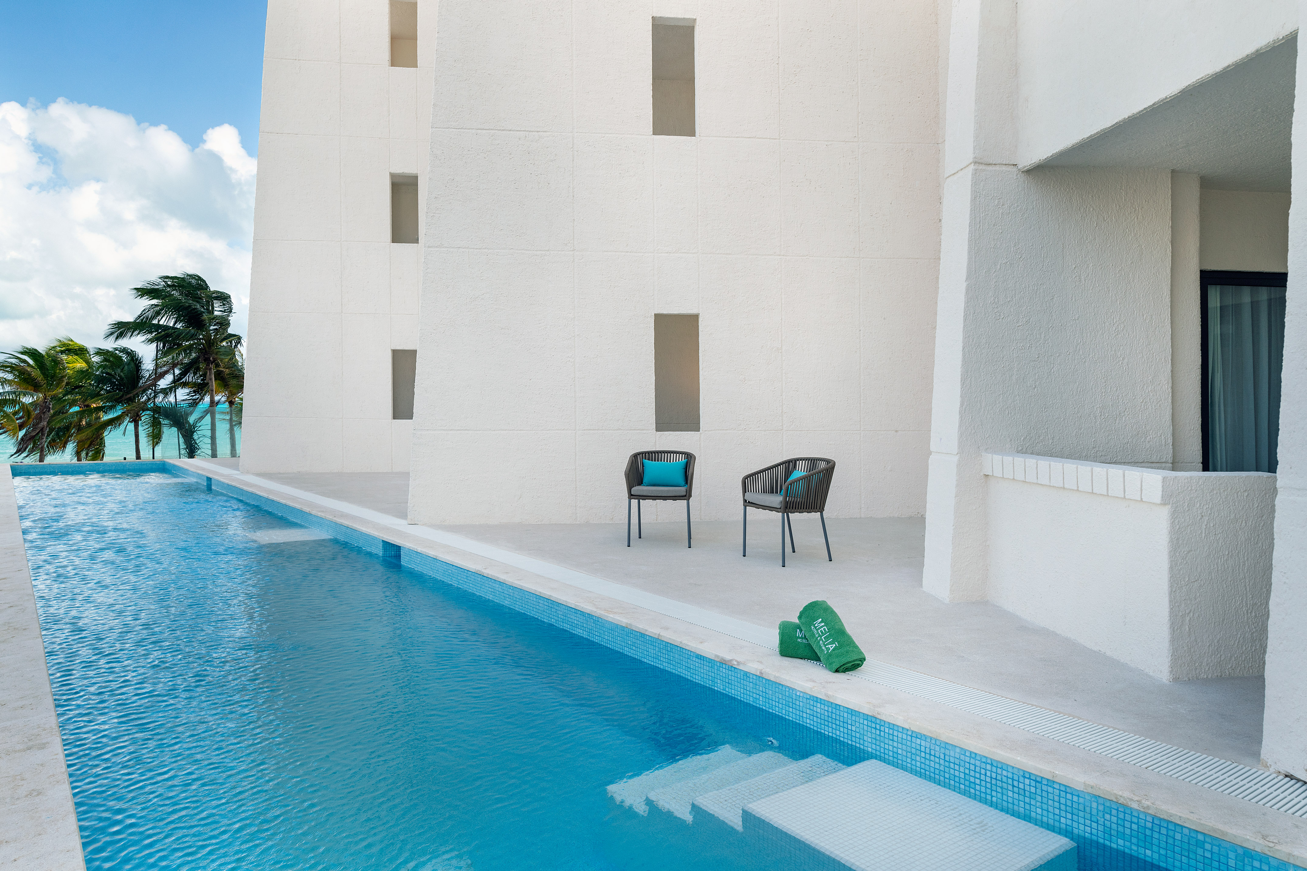 Modern Meliá resort pool and patio with ocean view and palm trees.