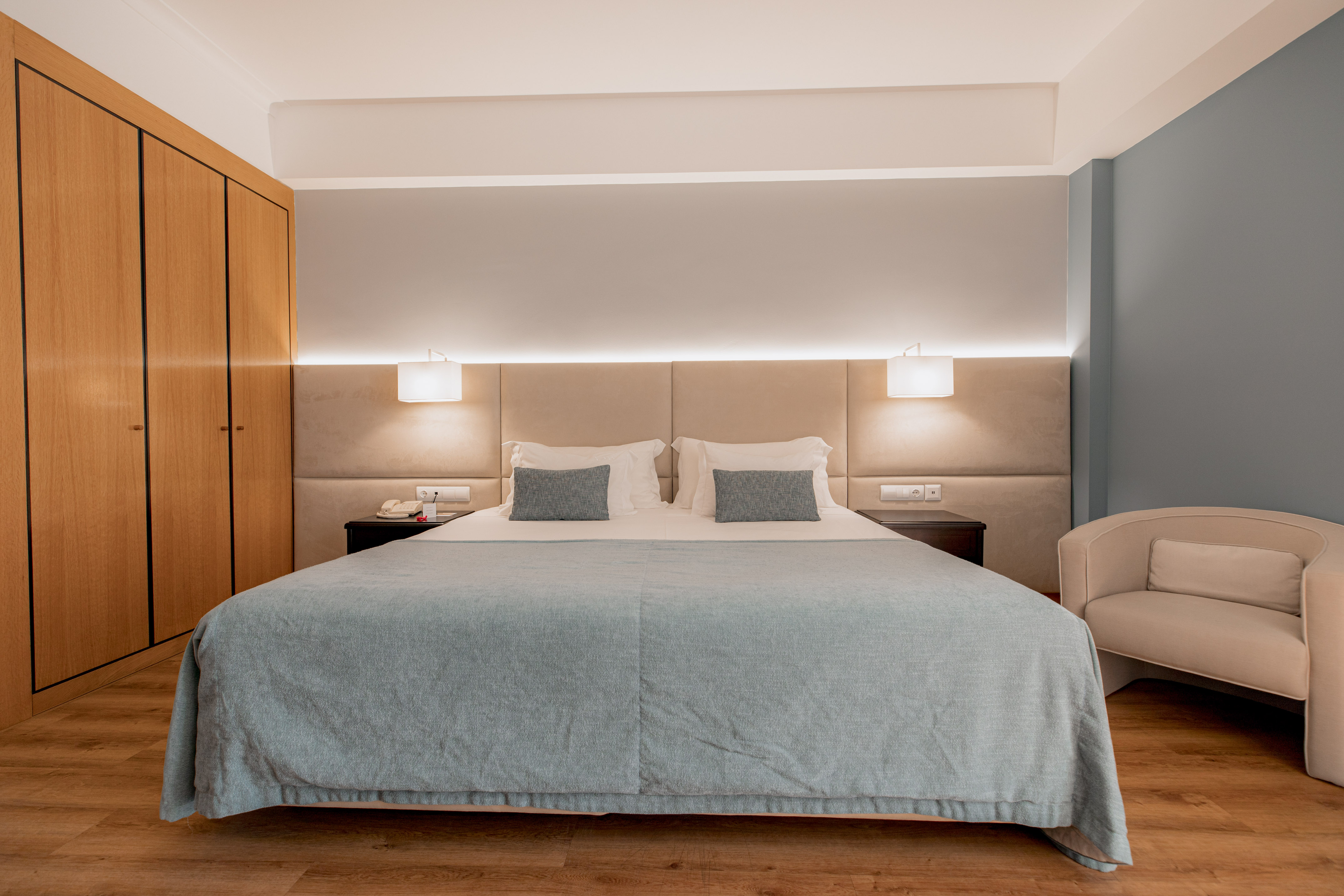Comfortable hotel bedroom with blue bed, wood wardrobe, and modern lighting.