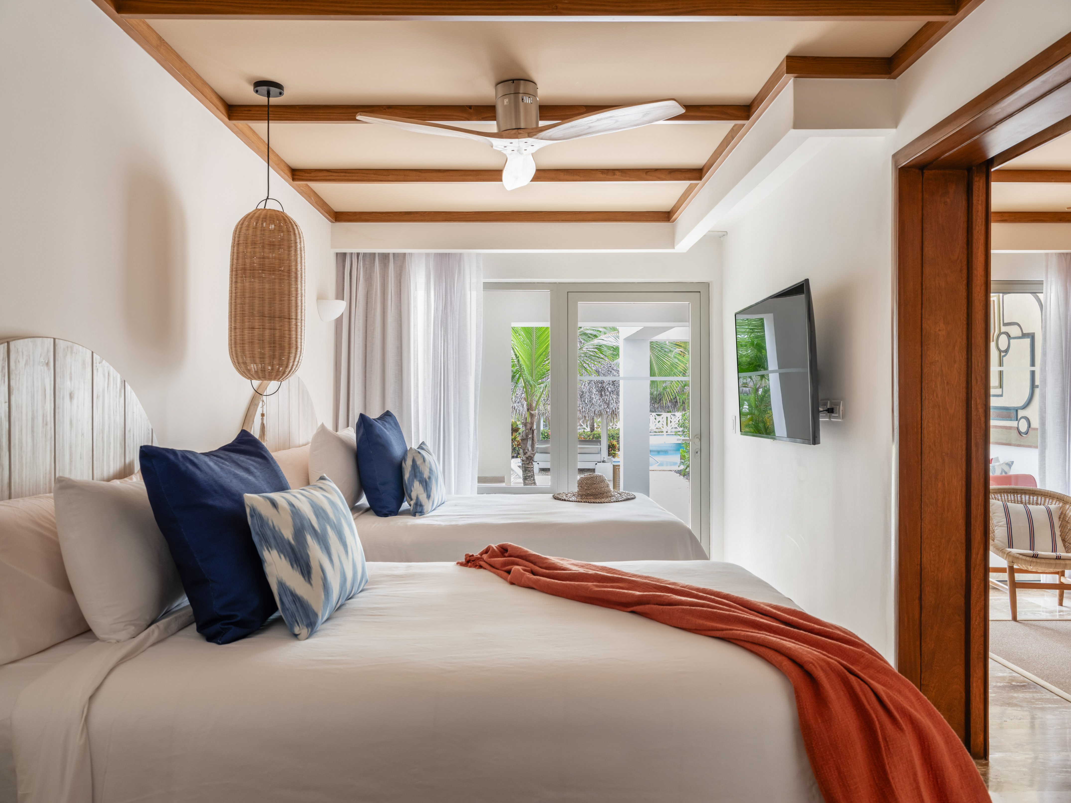 Modern tropical hotel room with twin beds, ceiling fan, and patio with pool view.