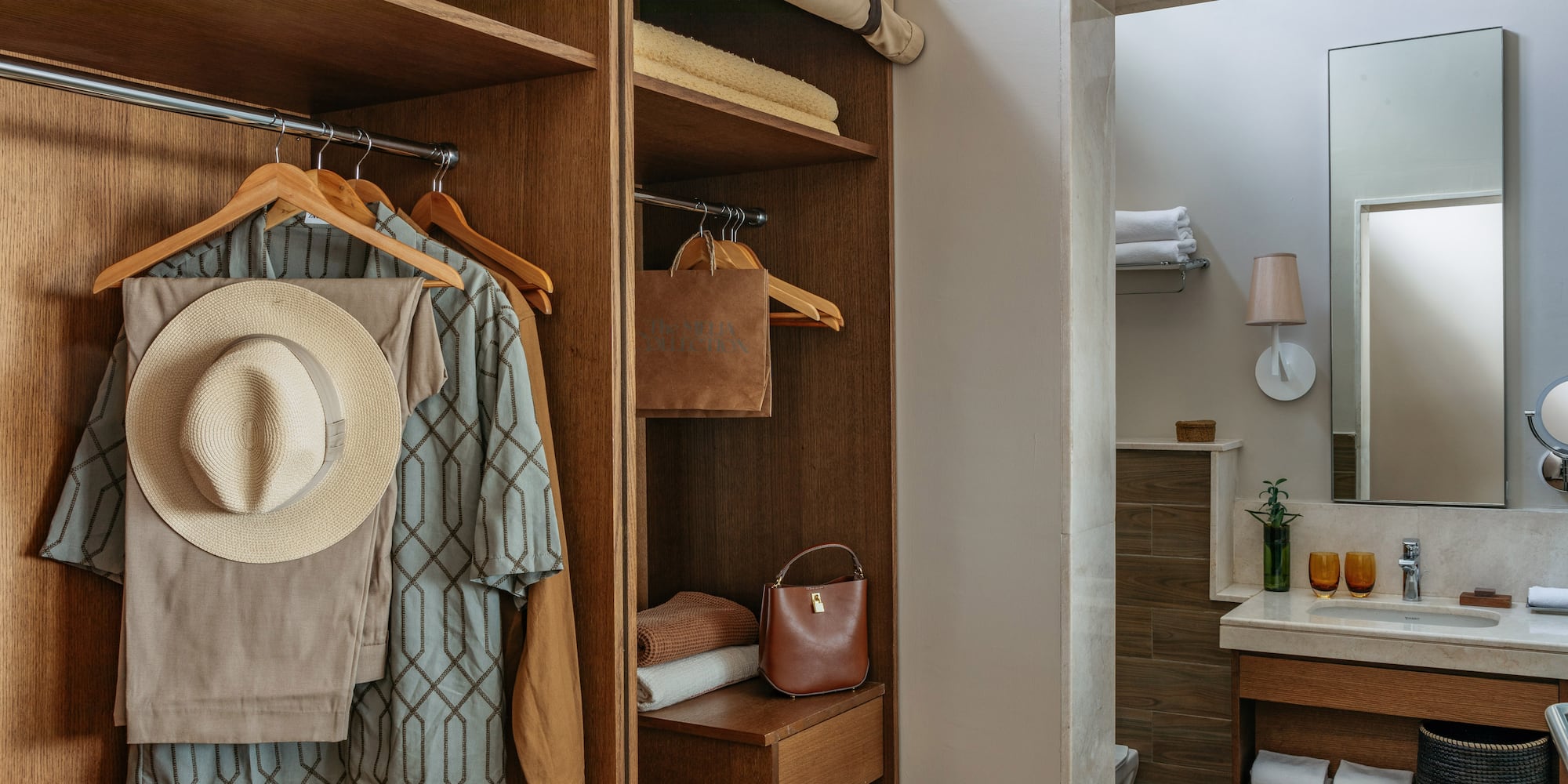 Wooden hotel closet with hanging clothes, hat, towels, and modern bathroom.