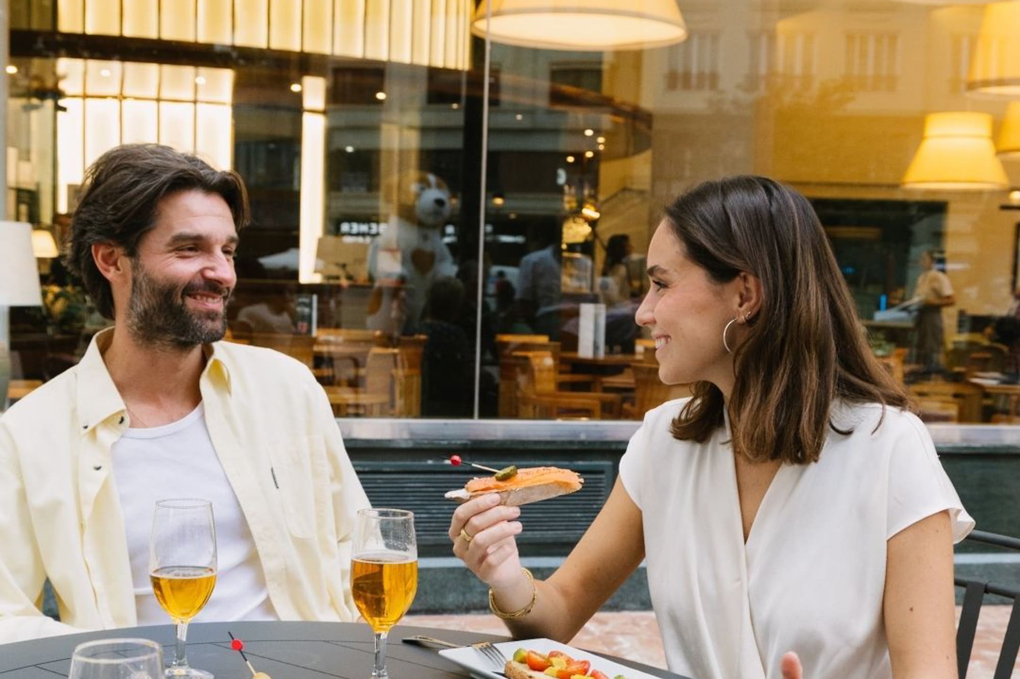 Couple smiling, enjoying tapas and beer at an outdoor restaurant.