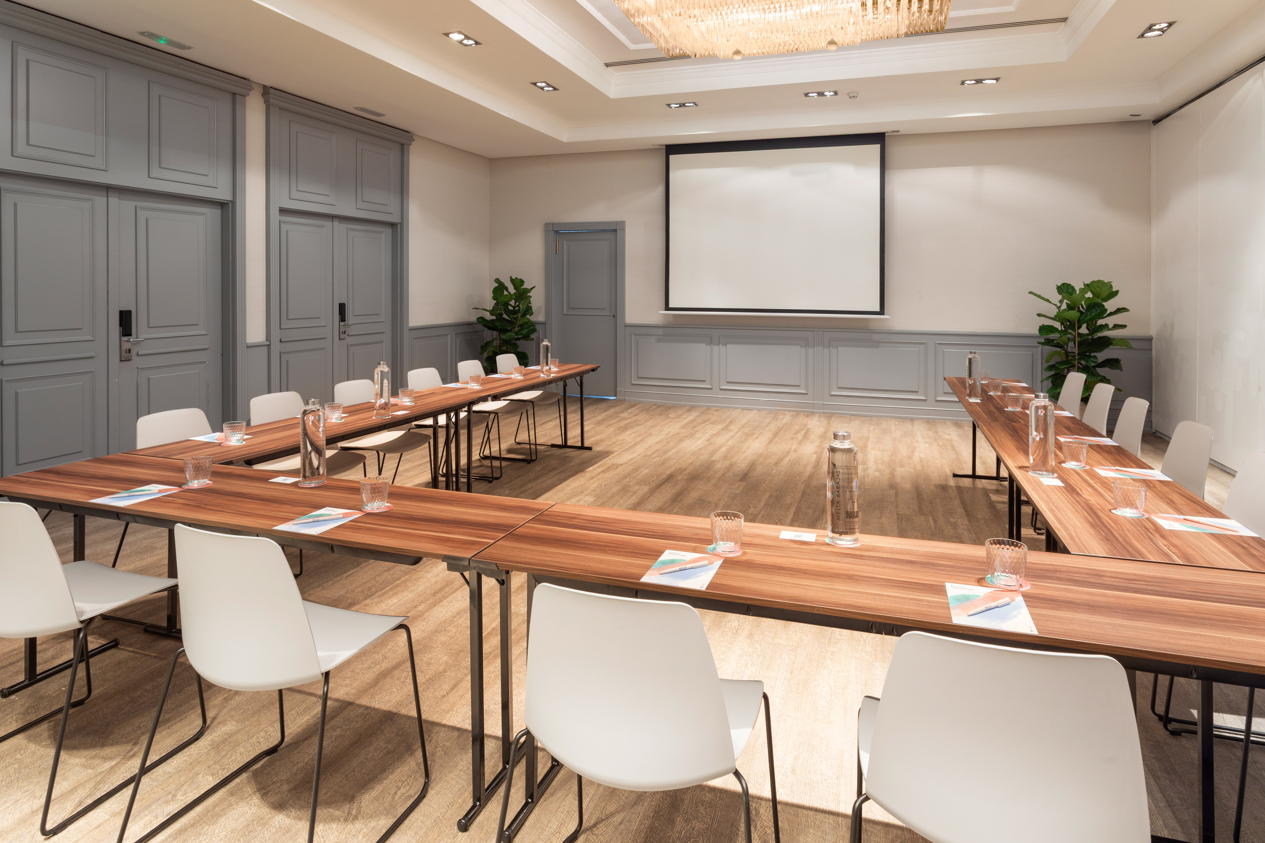 Elegant U-shaped conference room with white chairs and projector screen.