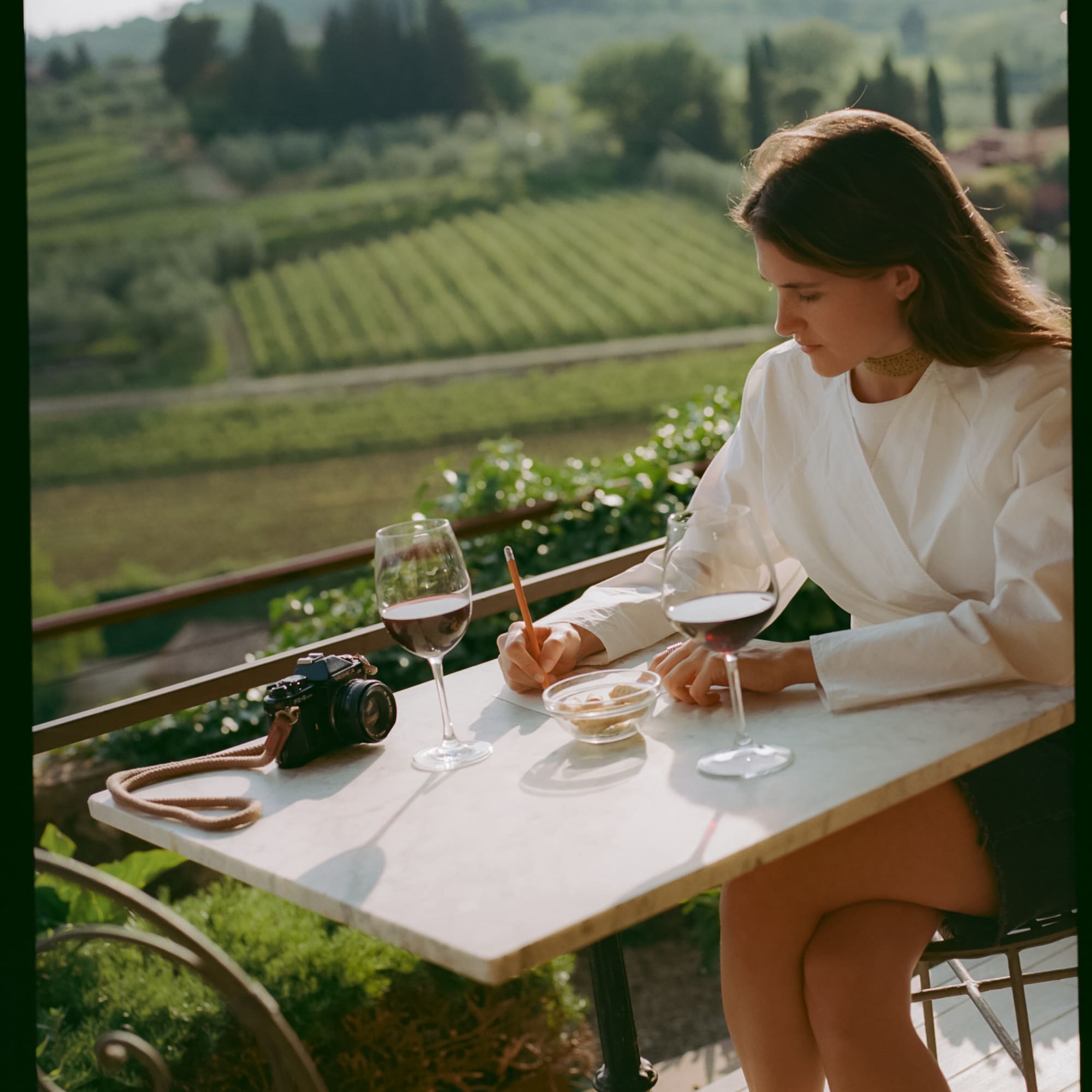 a woman sitting at a table with wine glasses and a camera