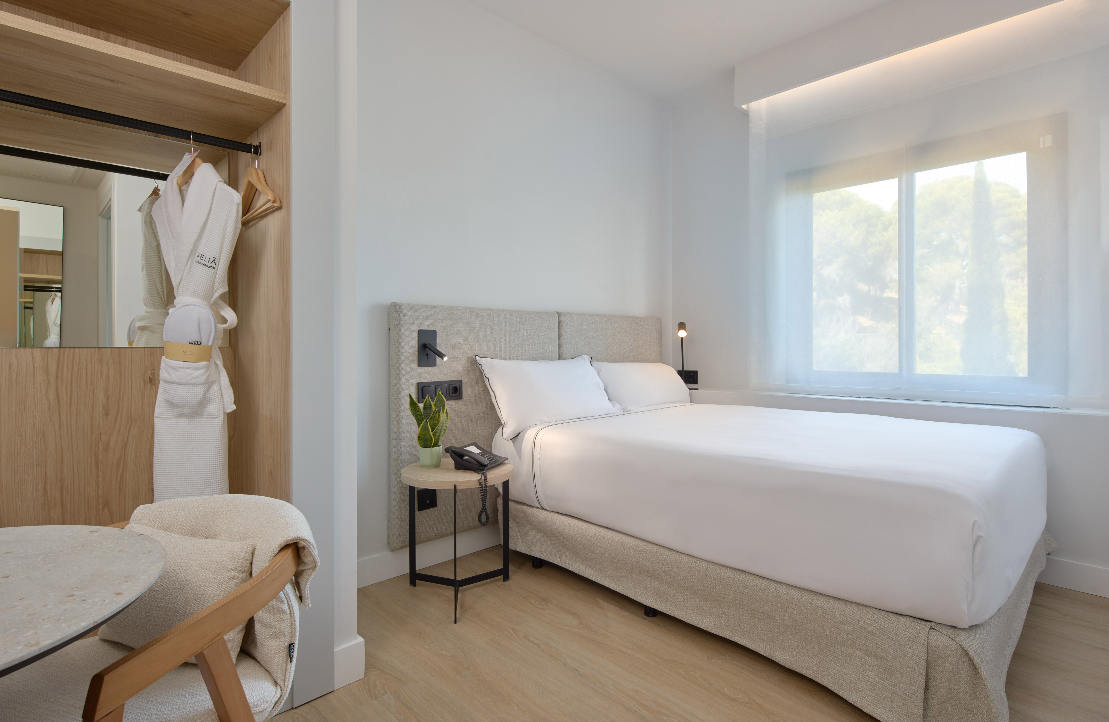 Modern hotel room with bed, wardrobe, bathrobe, and bright window view.