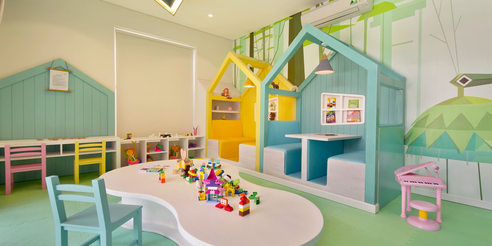 Colorful children's playroom with house booths, blocks, green forest mural.
