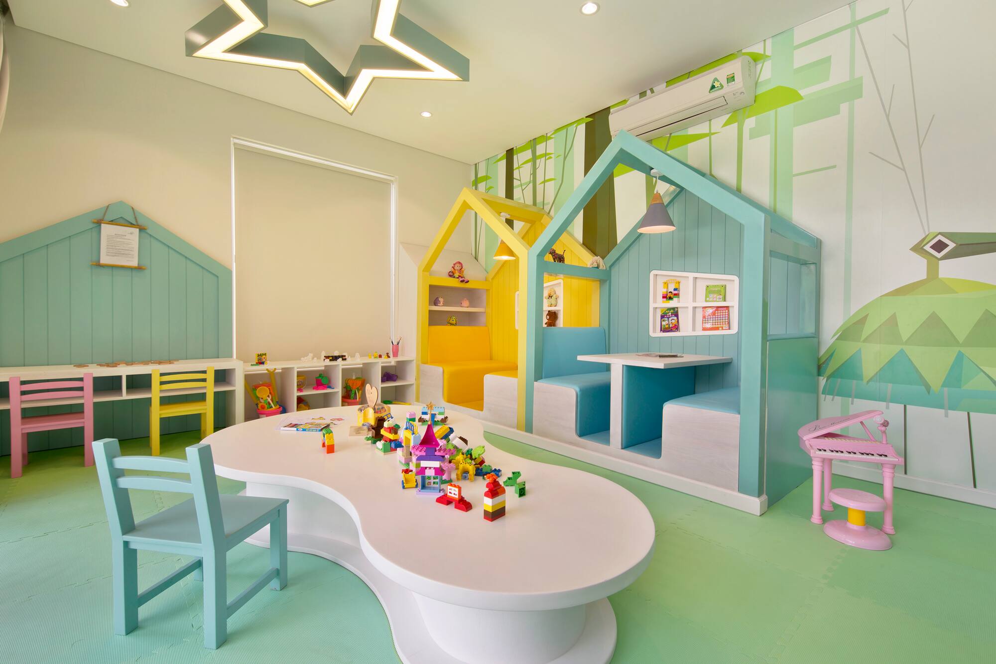 Colorful children's playroom with house booths, blocks, green forest mural.
