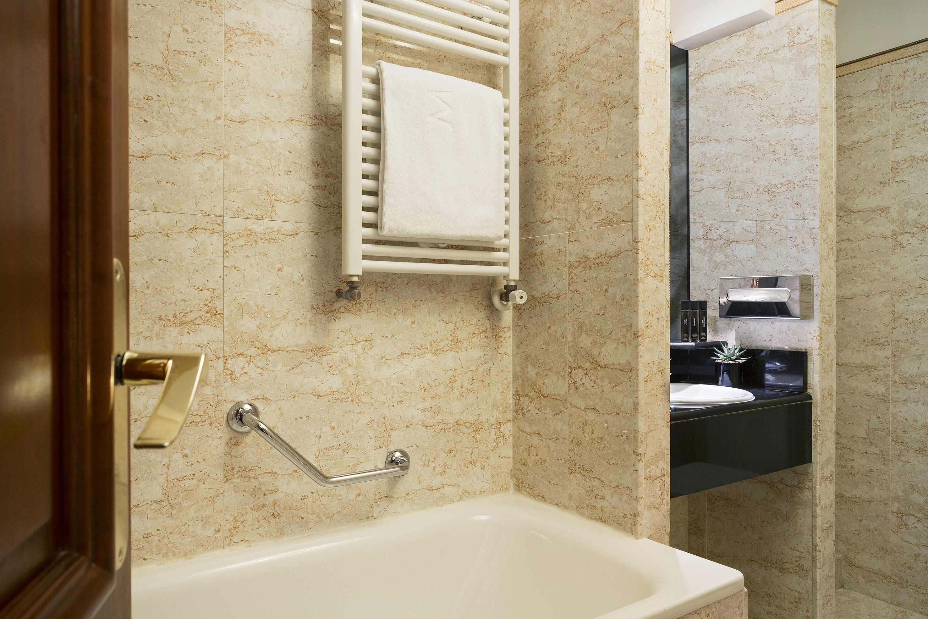 Accessible hotel bathroom with marble walls, bathtub, and towel warmer.