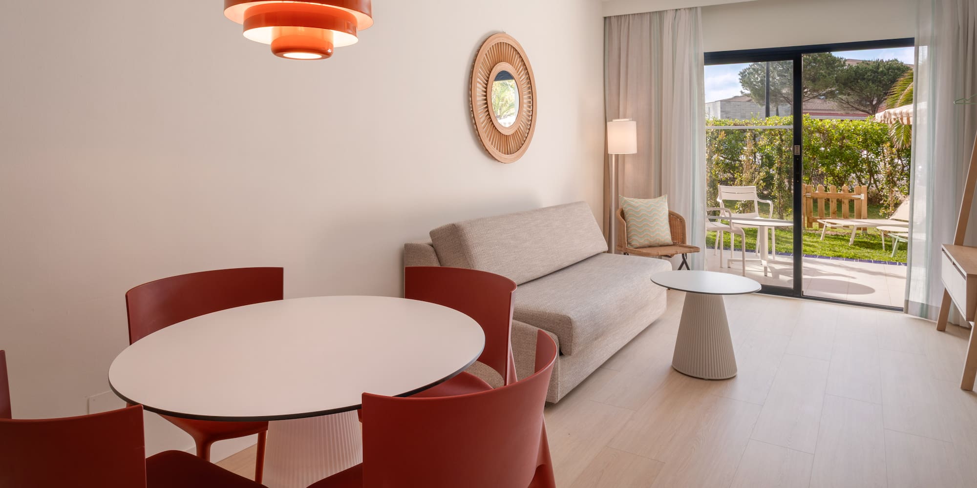Modern hotel suite with dining area, sofa, and patio garden view.