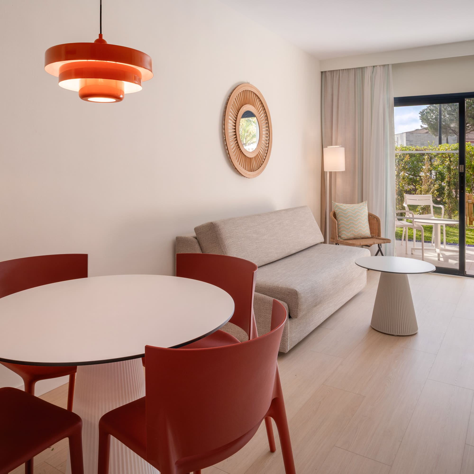 Modern hotel suite with dining area, sofa, and patio garden view.