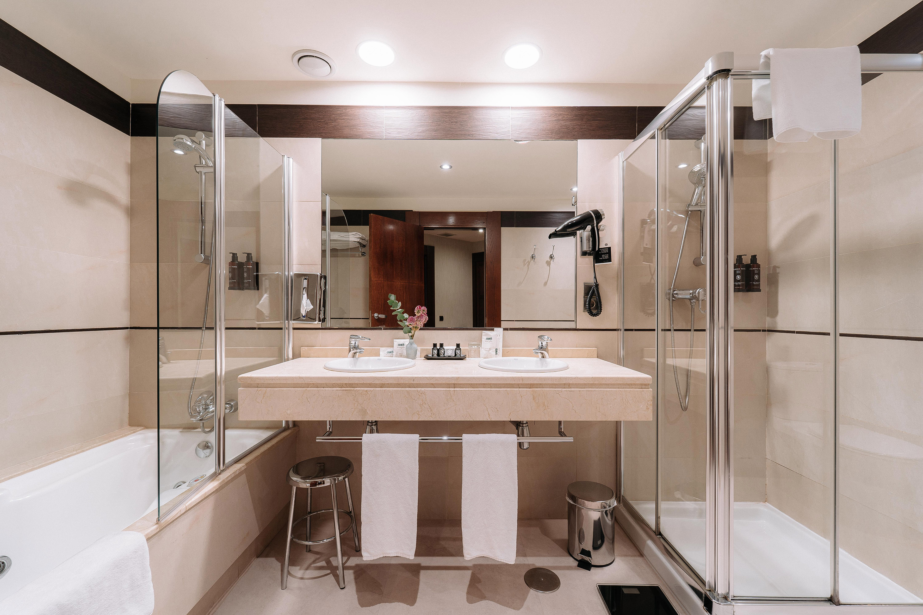 Modern hotel bathroom with double vanity, bathtub, and glass shower.