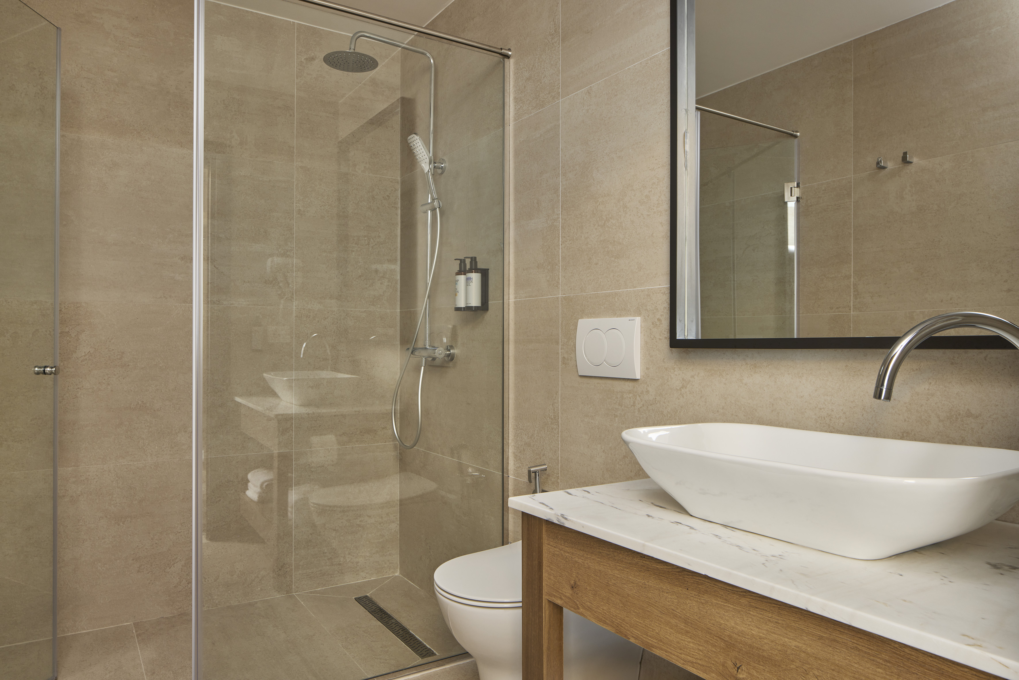 Modern bathroom with walk-in shower, vessel sink, and beige tile.