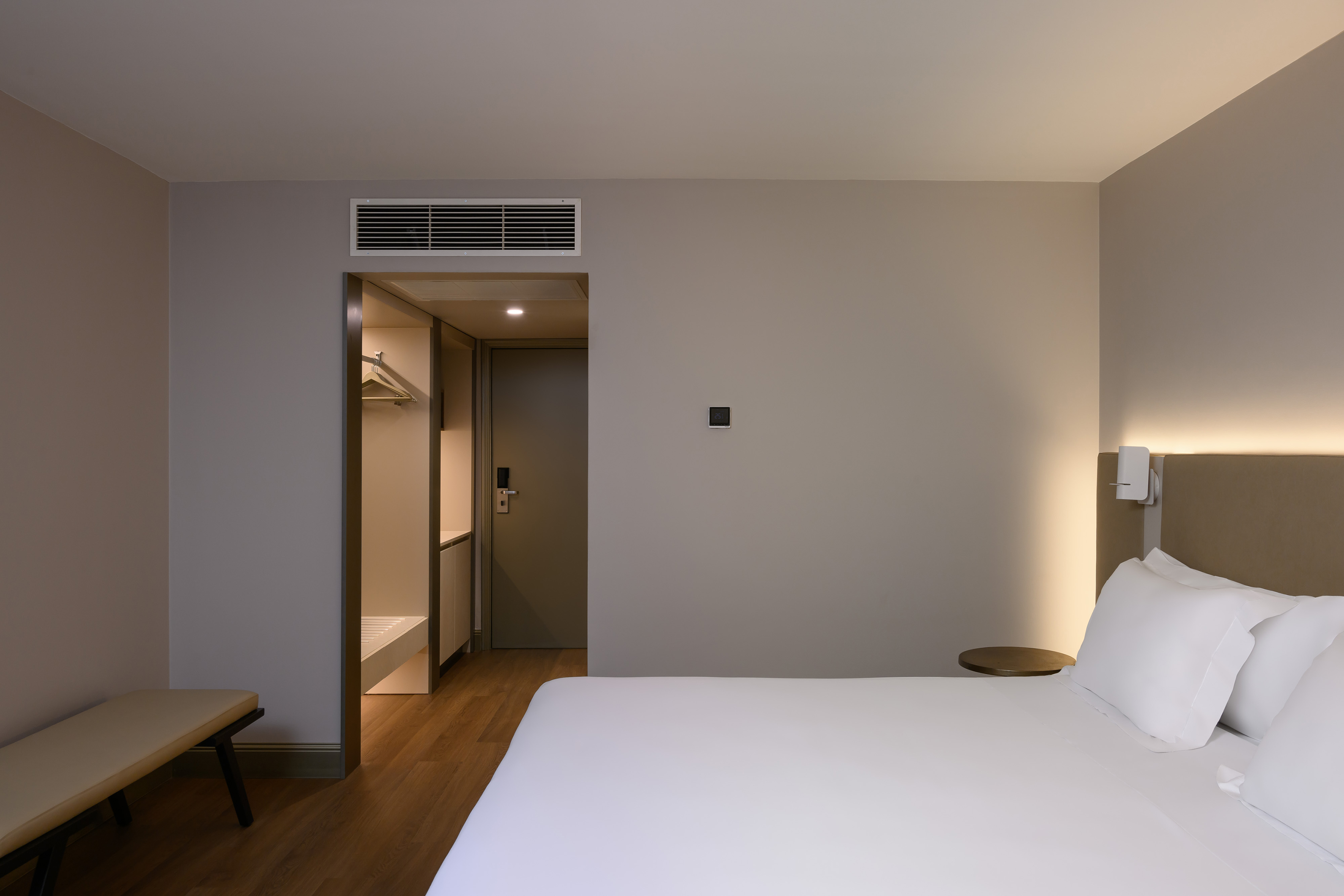 Hotel bedroom with white bed, integrated headboard light, and open closet.