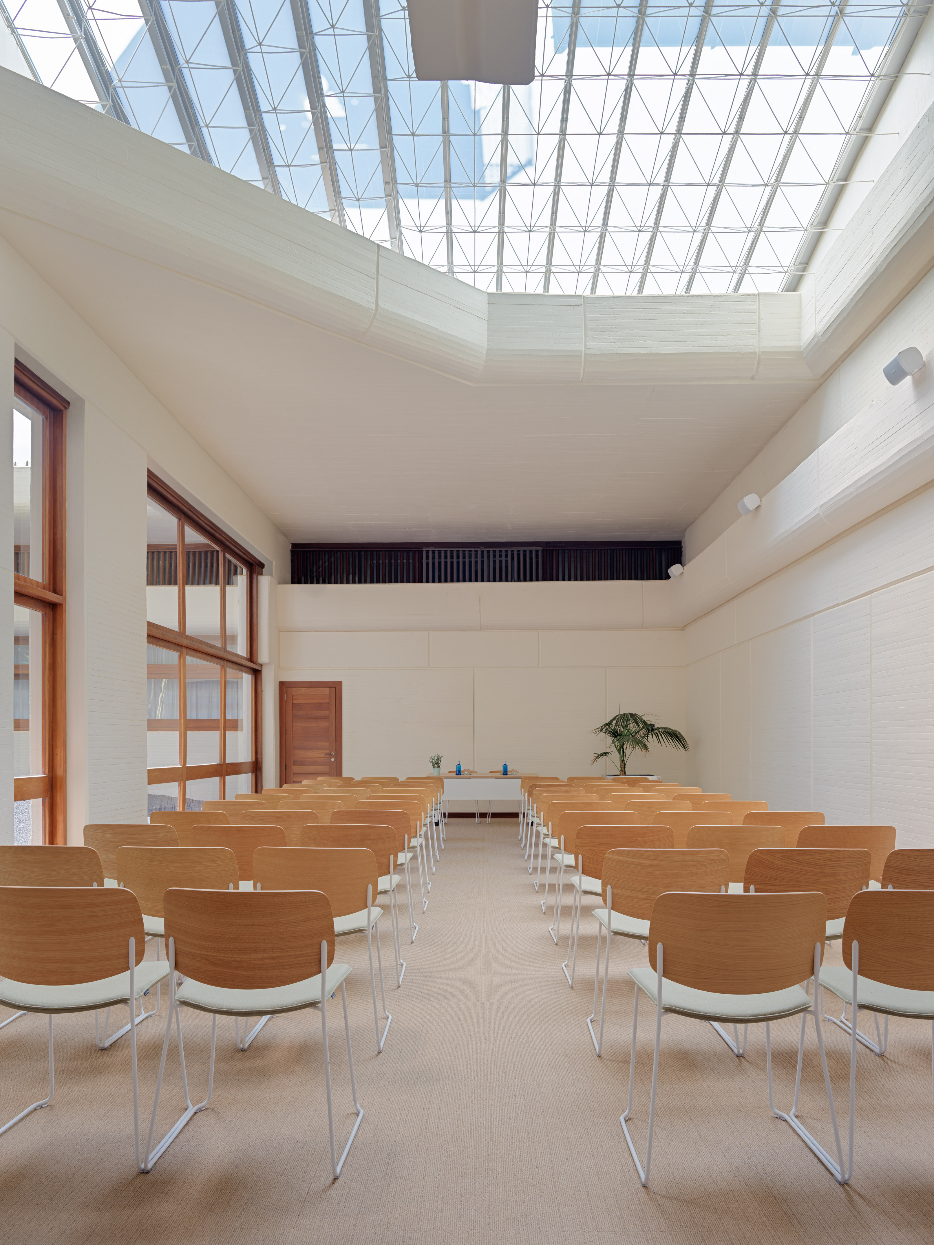 Spacious meeting room with skylight, modern wood chairs, white walls, and beige carpet.