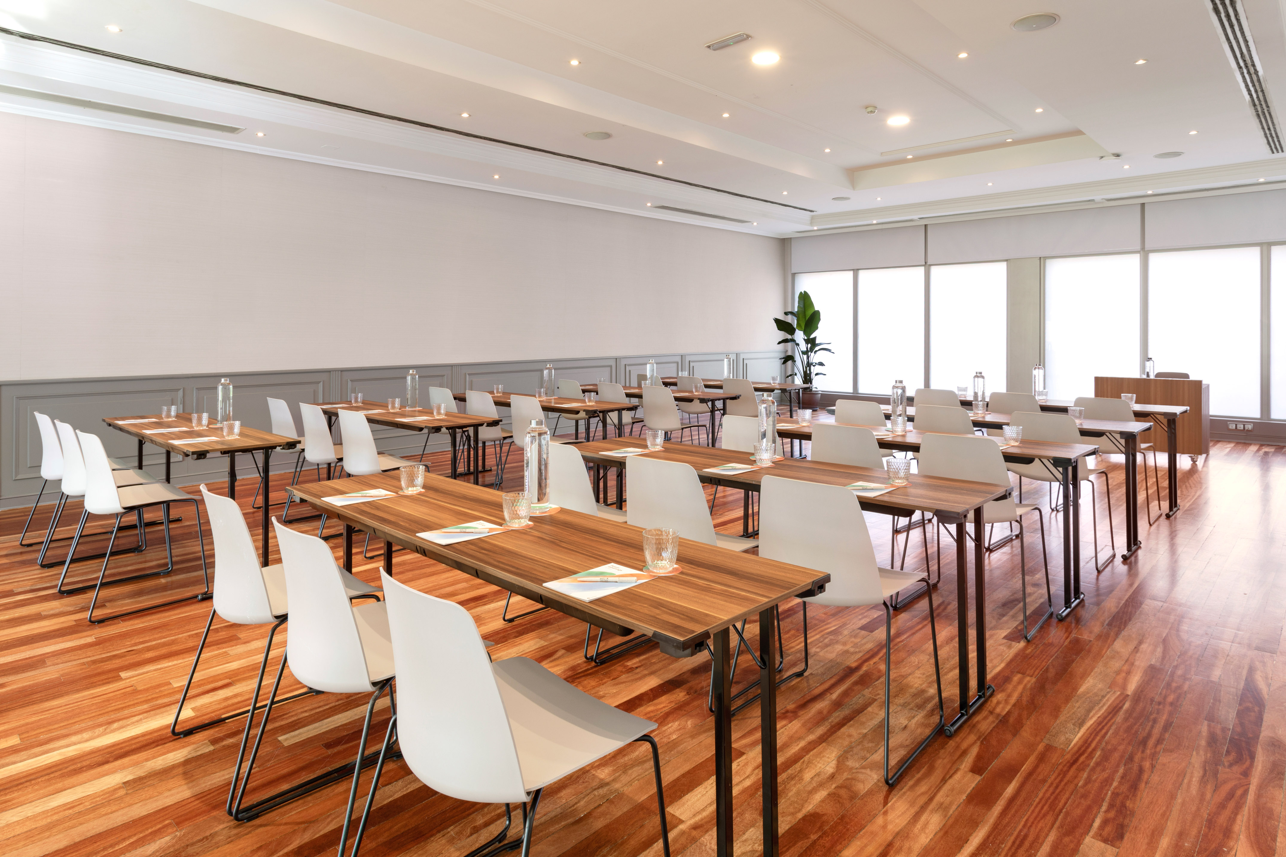 Classroom style conference room with wooden tables, white chairs, and hardwood floor.