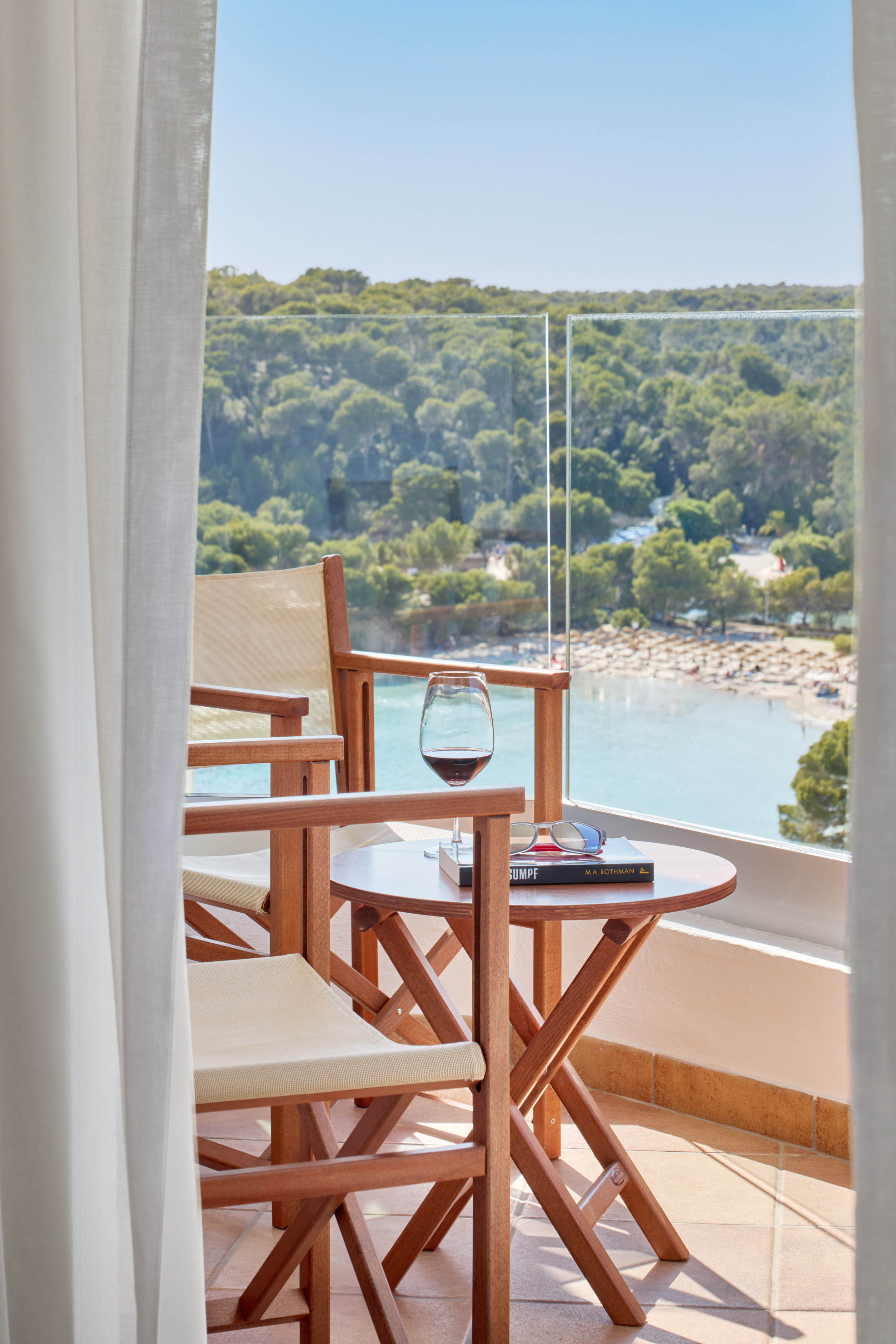 Balcony with sea view, chairs, wine, book, overlooking beach and green forest.