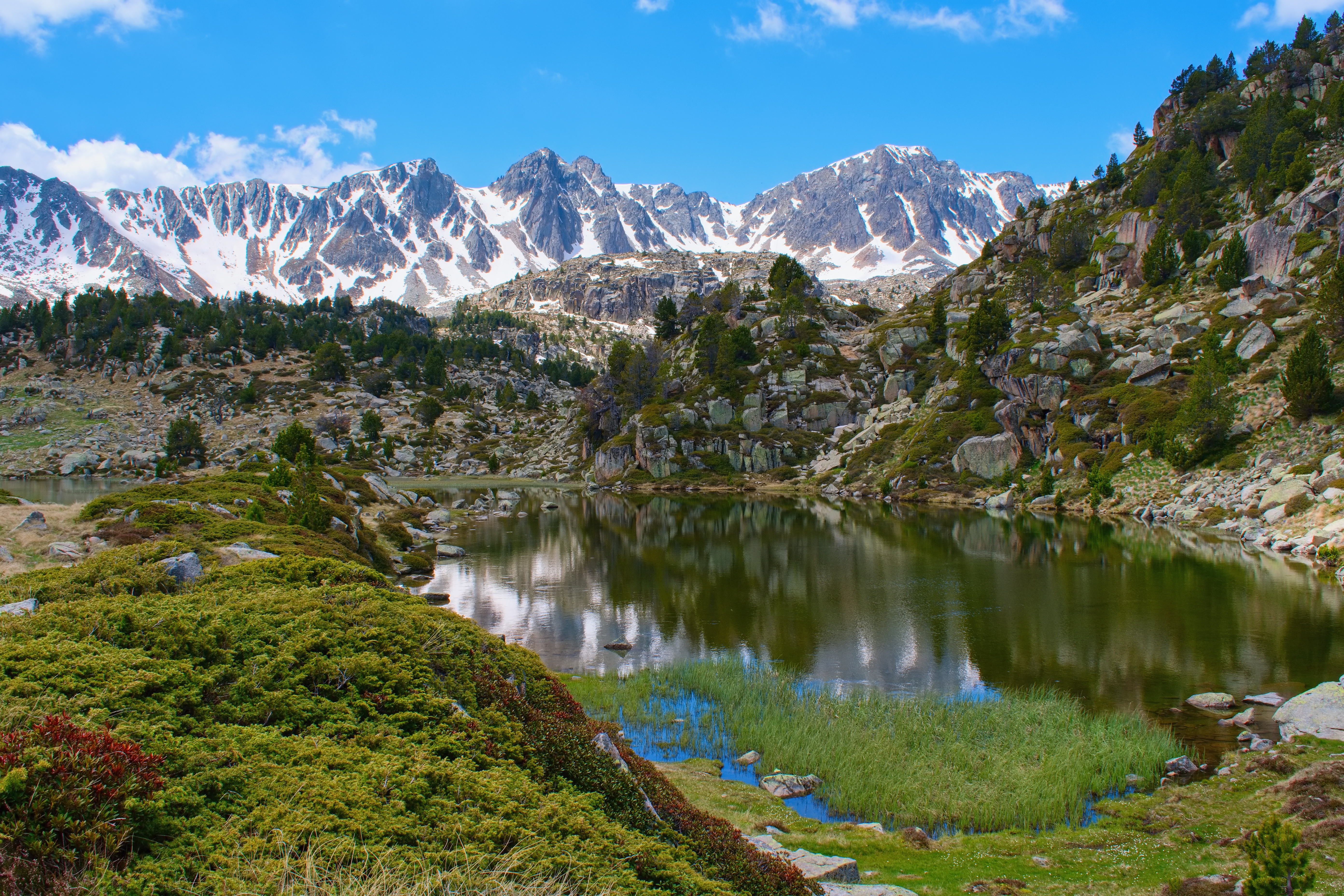 Snowy mountains reflecting in a clear alpine lake with green rocky slopes.