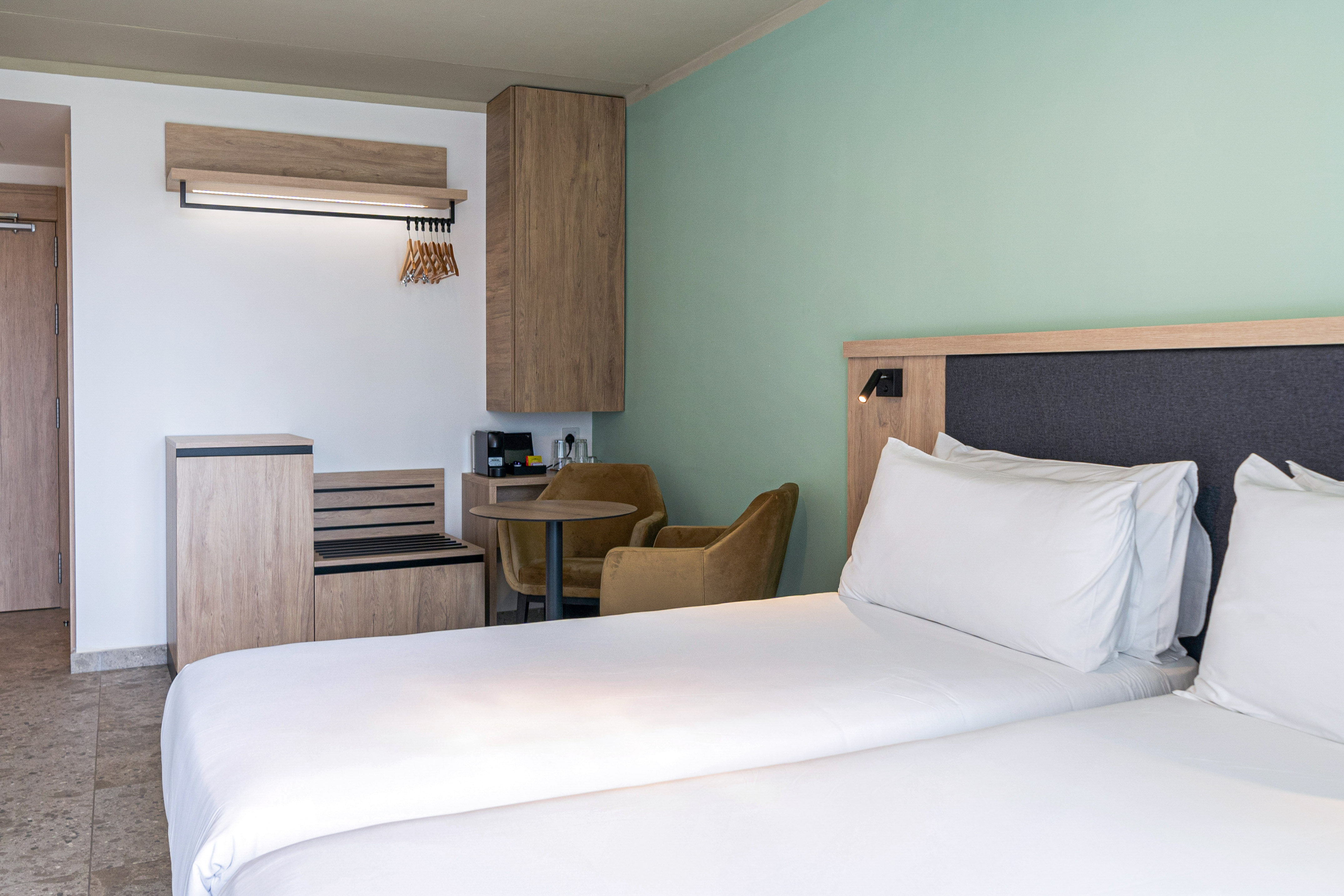 Clean, modern hotel room with twin beds, green wall, and wood furniture.