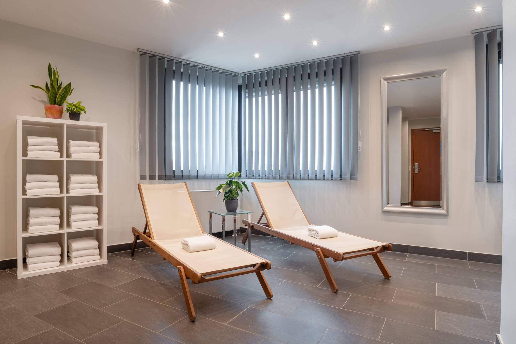 Wellness lounge with two wooden chairs, white towels, potted plants, and tiled floor.
