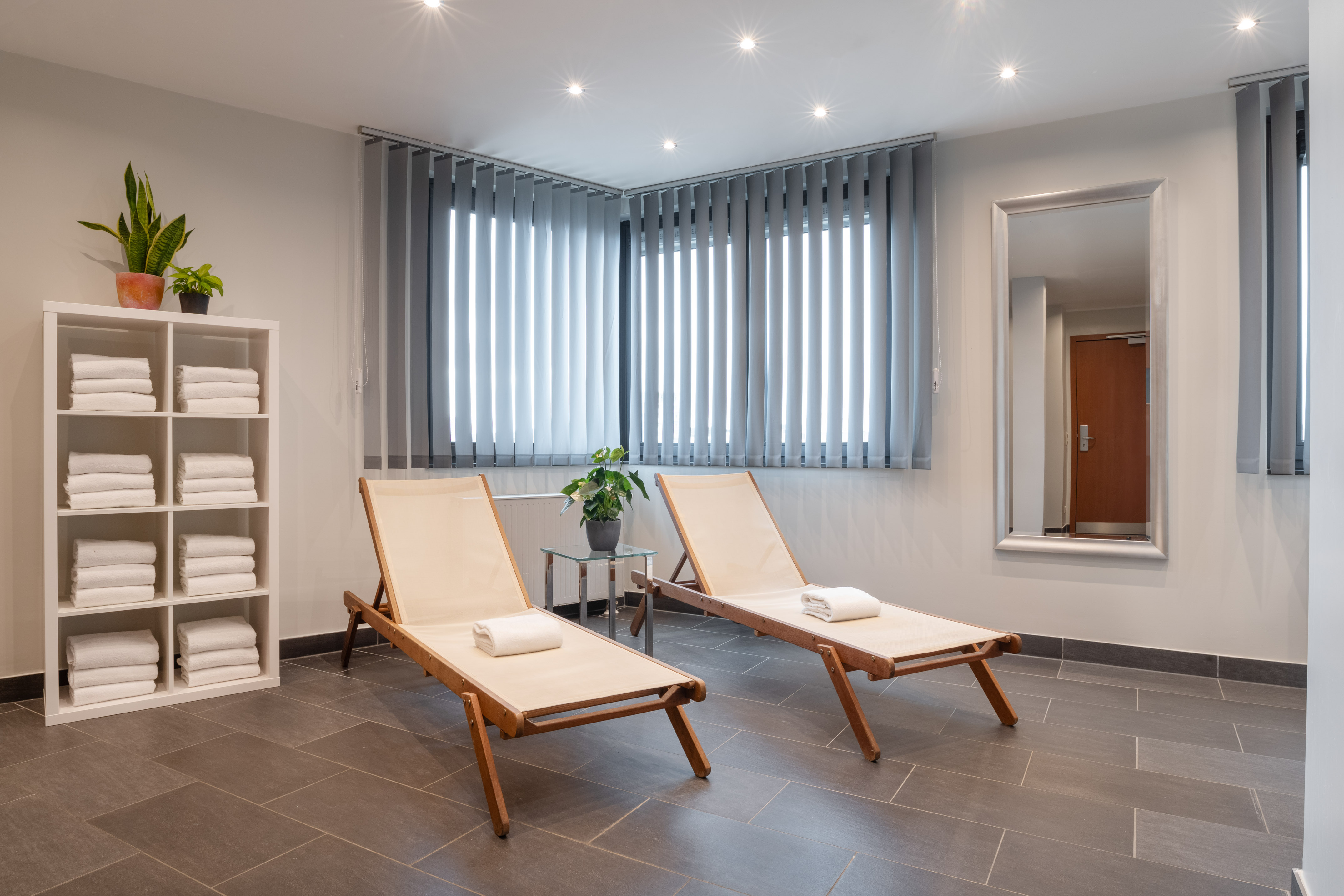 Wellness lounge with two wooden chairs, white towels, potted plants, and tiled floor.