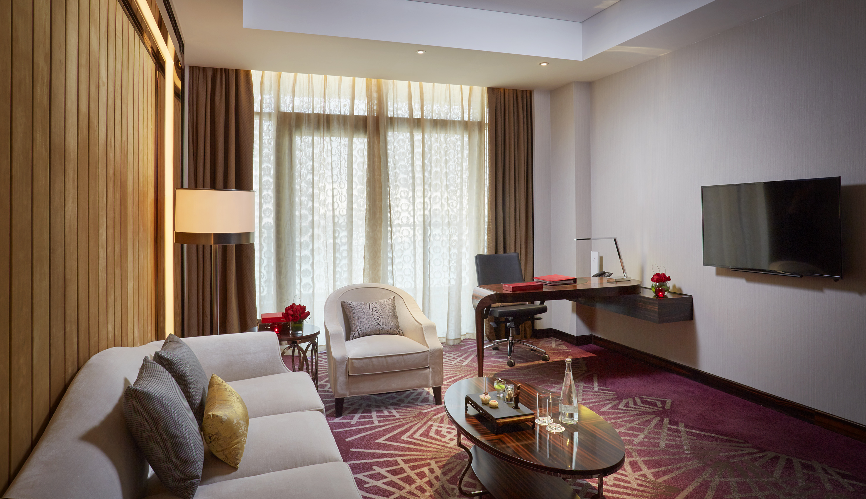 Modern hotel suite living room with sofa, armchair, work desk, and TV.
