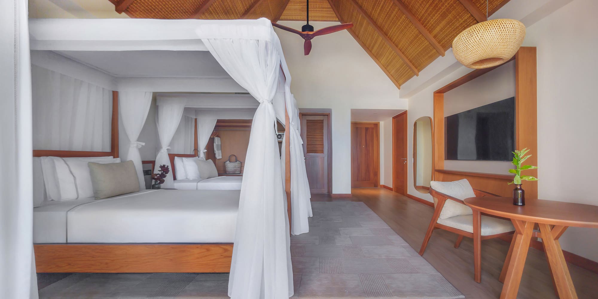 Tropical hotel room with canopy bed, vaulted thatched ceiling, and modern decor.