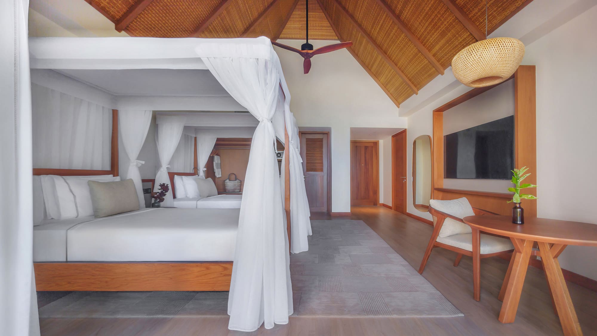 Tropical hotel room with canopy bed, vaulted thatched ceiling, and modern decor.