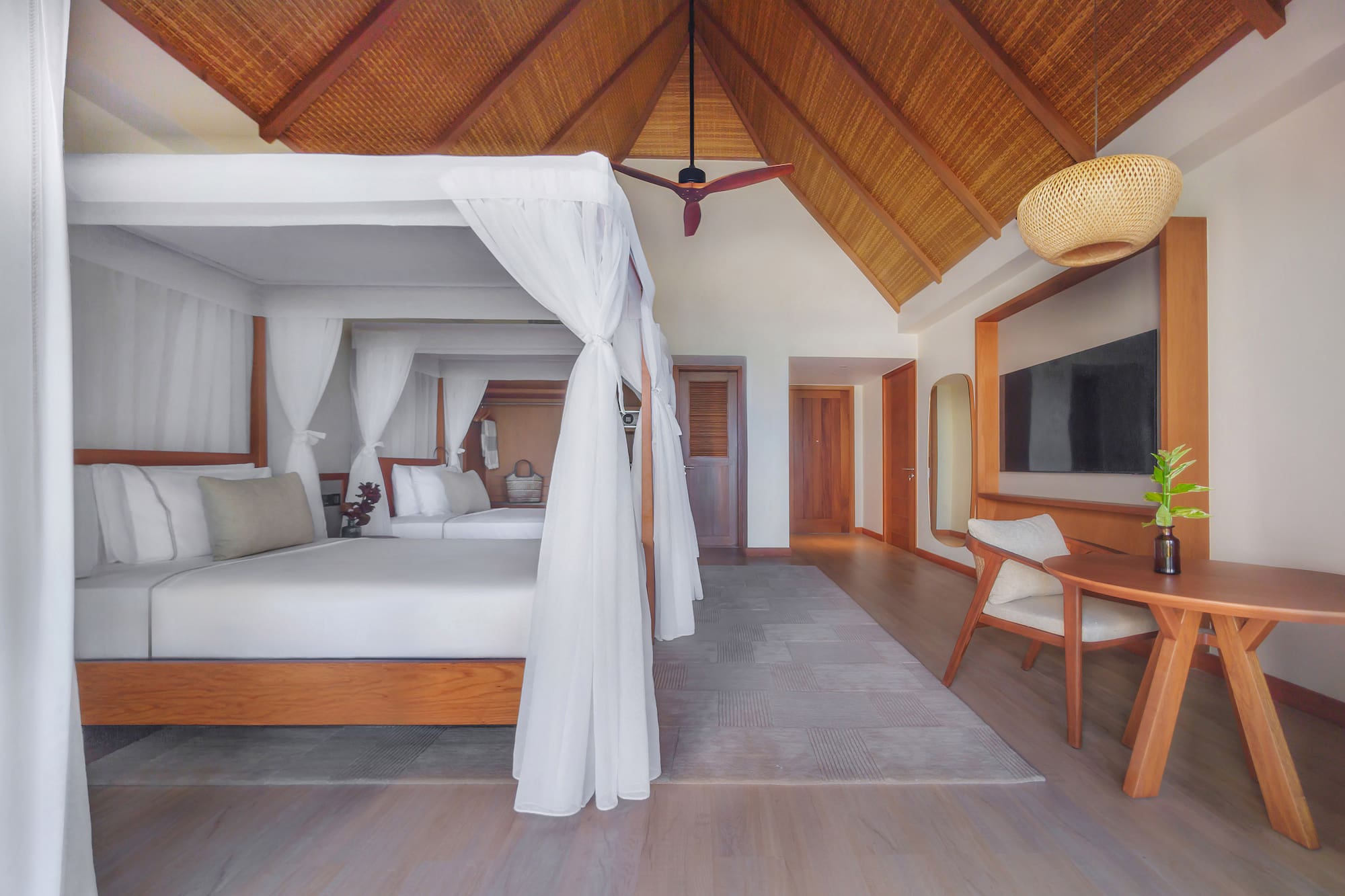 Tropical hotel room with canopy bed, vaulted thatched ceiling, and modern decor.