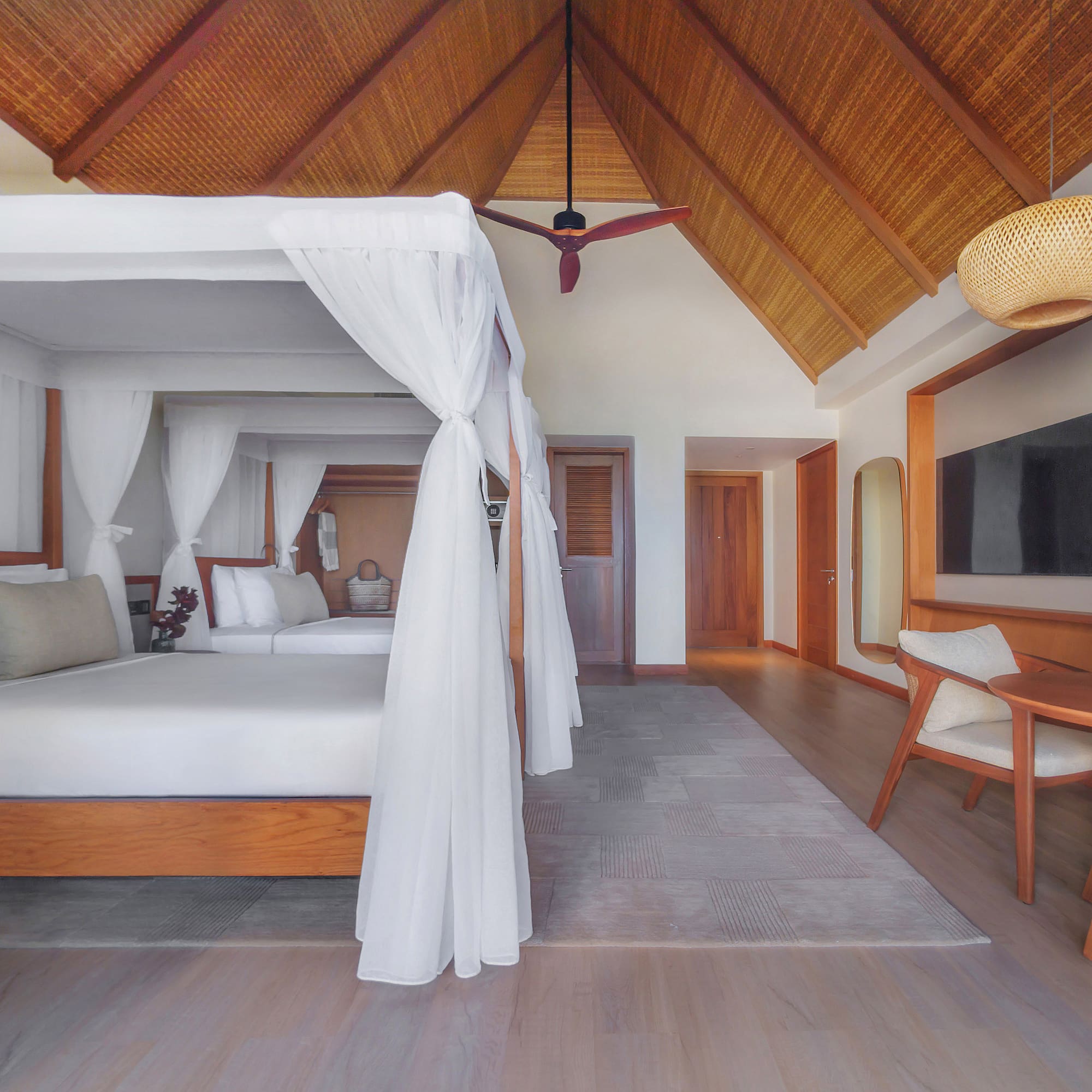 Tropical hotel room with canopy bed, vaulted thatched ceiling, and modern decor.