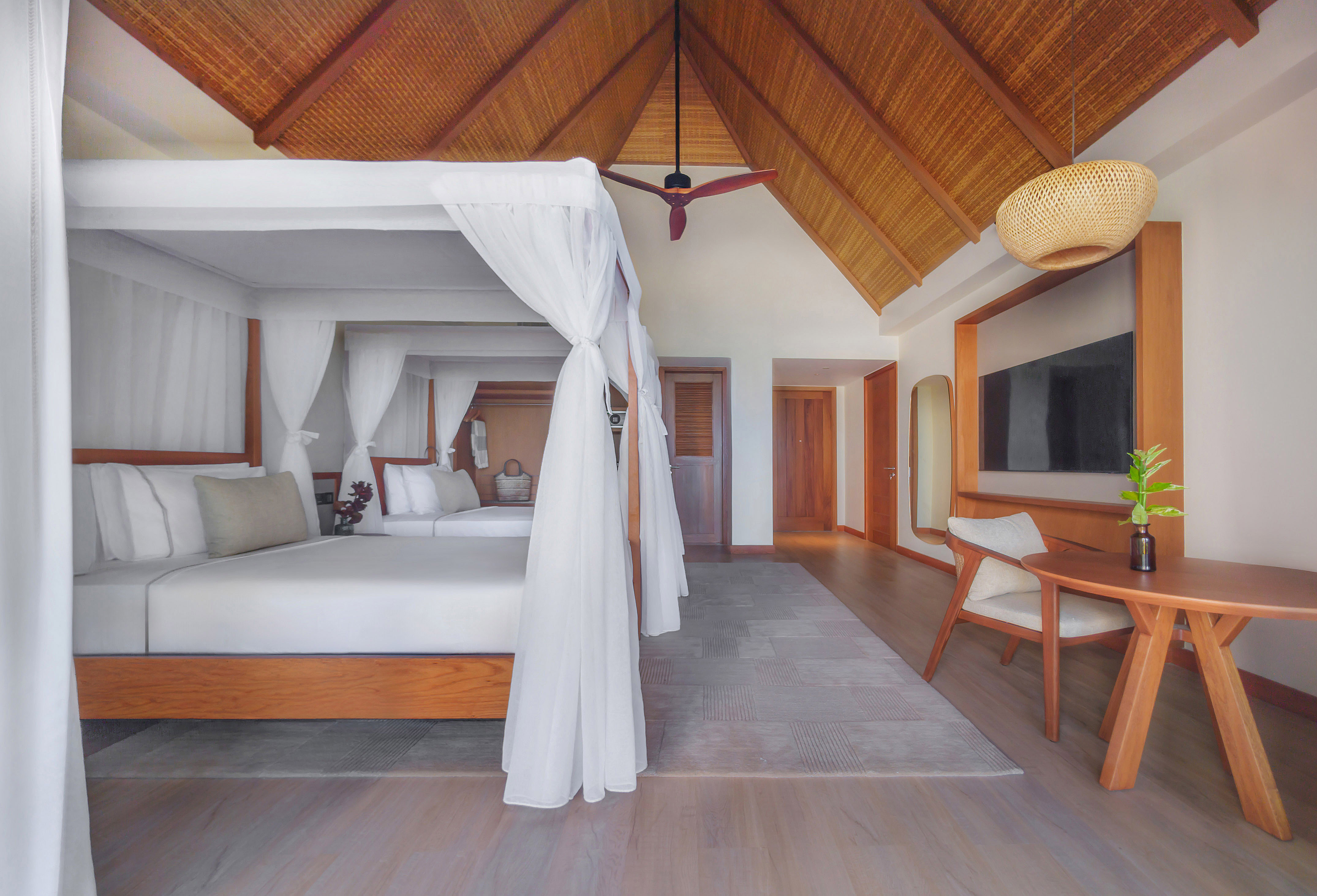 Tropical hotel room with canopy bed, vaulted thatched ceiling, and modern decor.