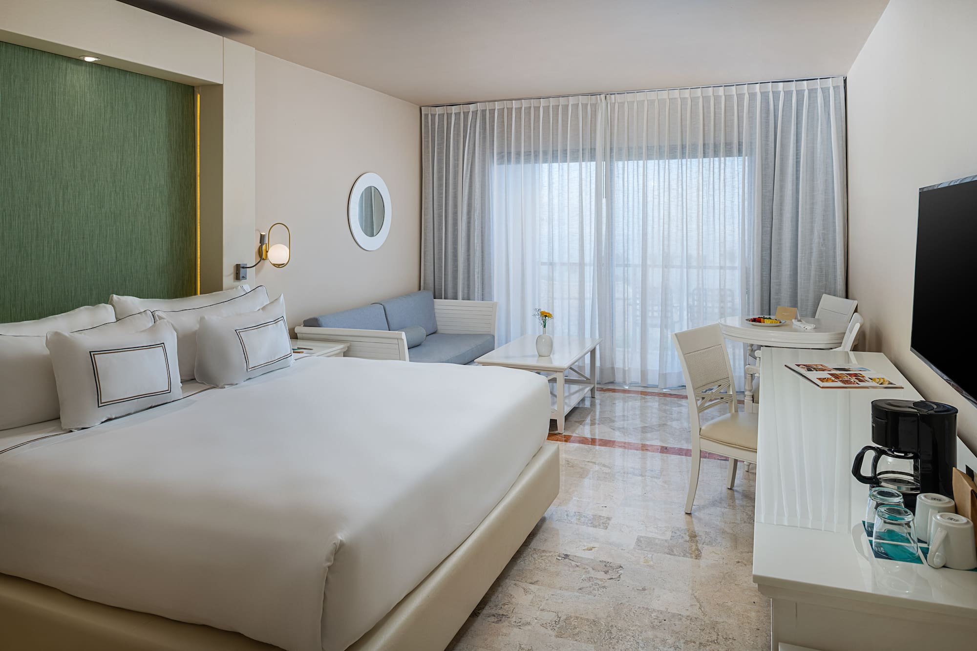 Modern hotel room with king bed, sofa, dining area, and large window.