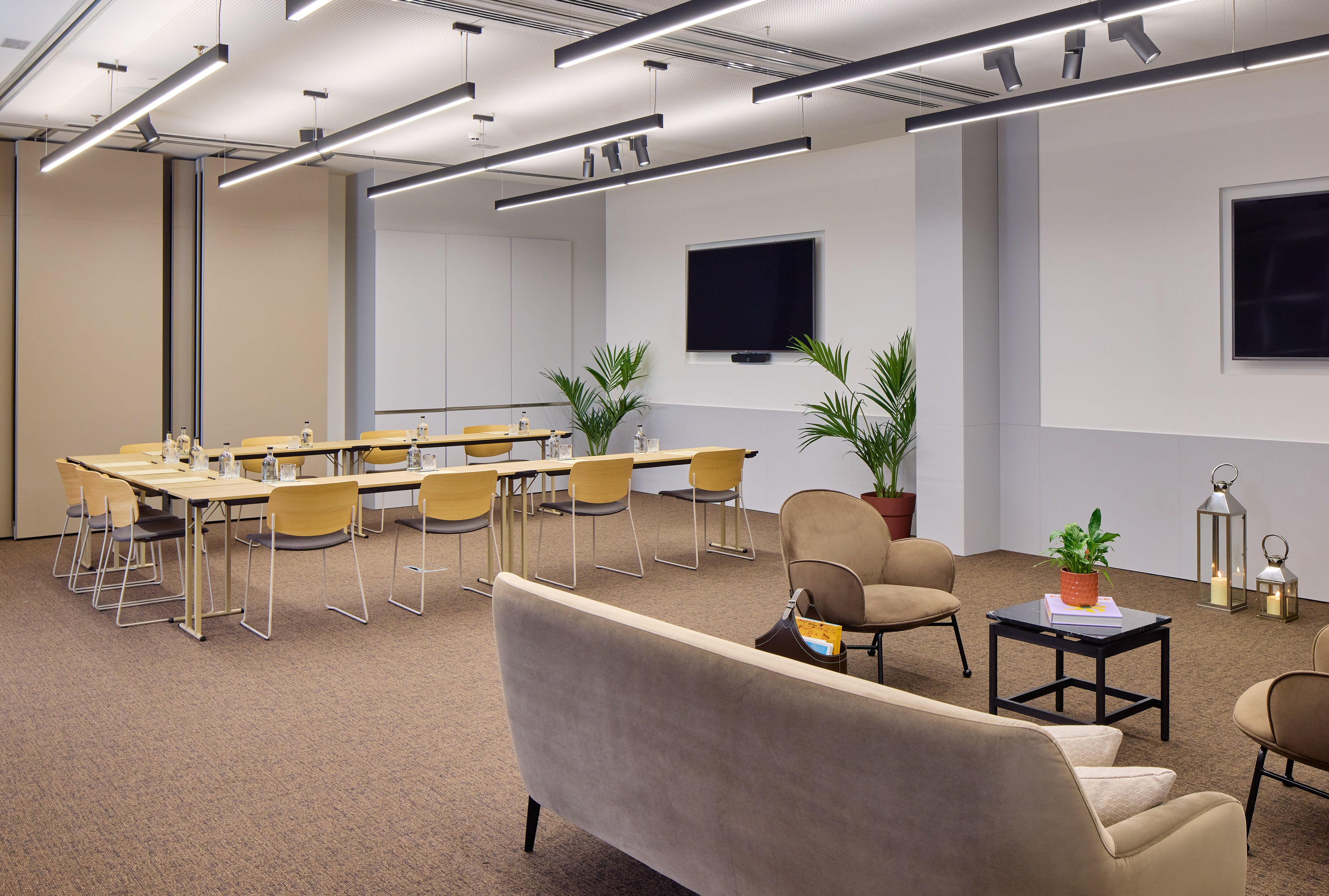 Flexible modern meeting space with conference tables, lounge, TV, and plants.