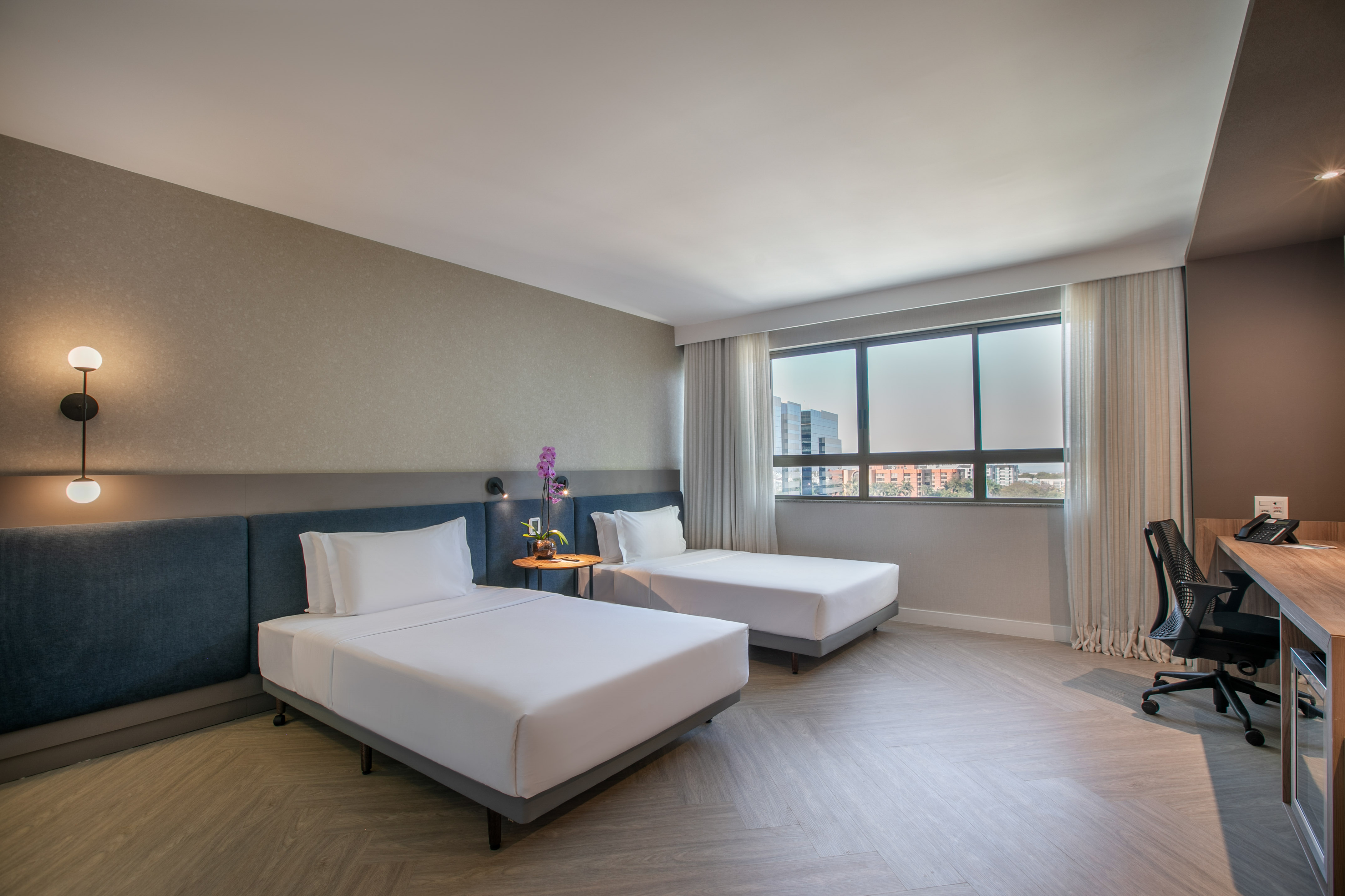 Modern twin bed hotel guest room with city view window and work desk.