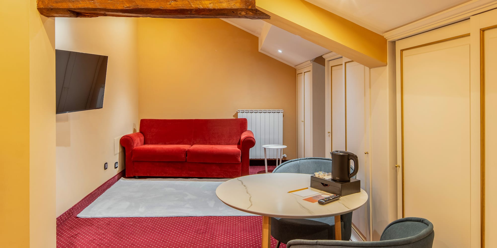 Attic hotel room with red sofa, TV, round table, and built-in wardrobes.