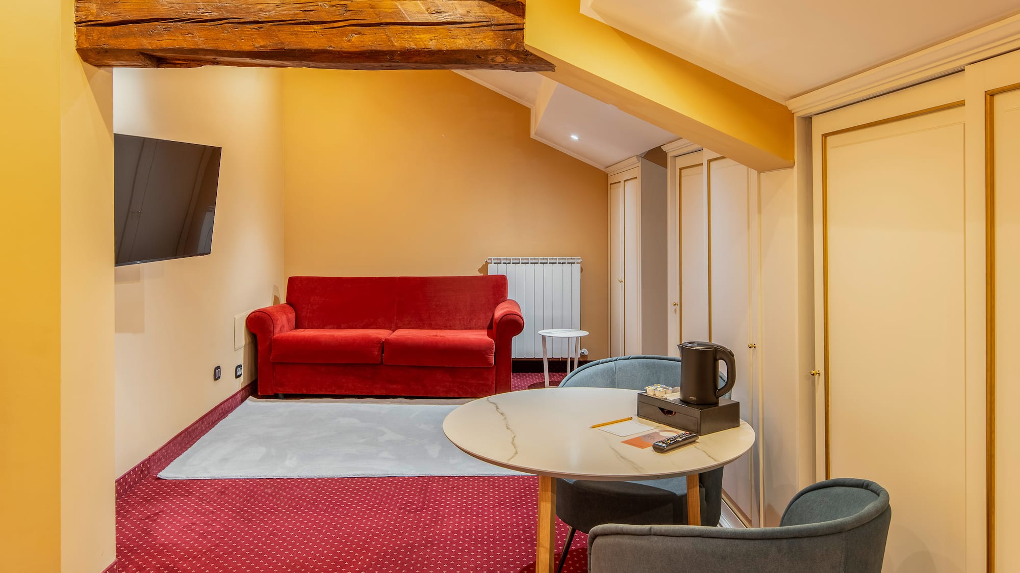 Attic hotel room with red sofa, TV, round table, and built-in wardrobes.
