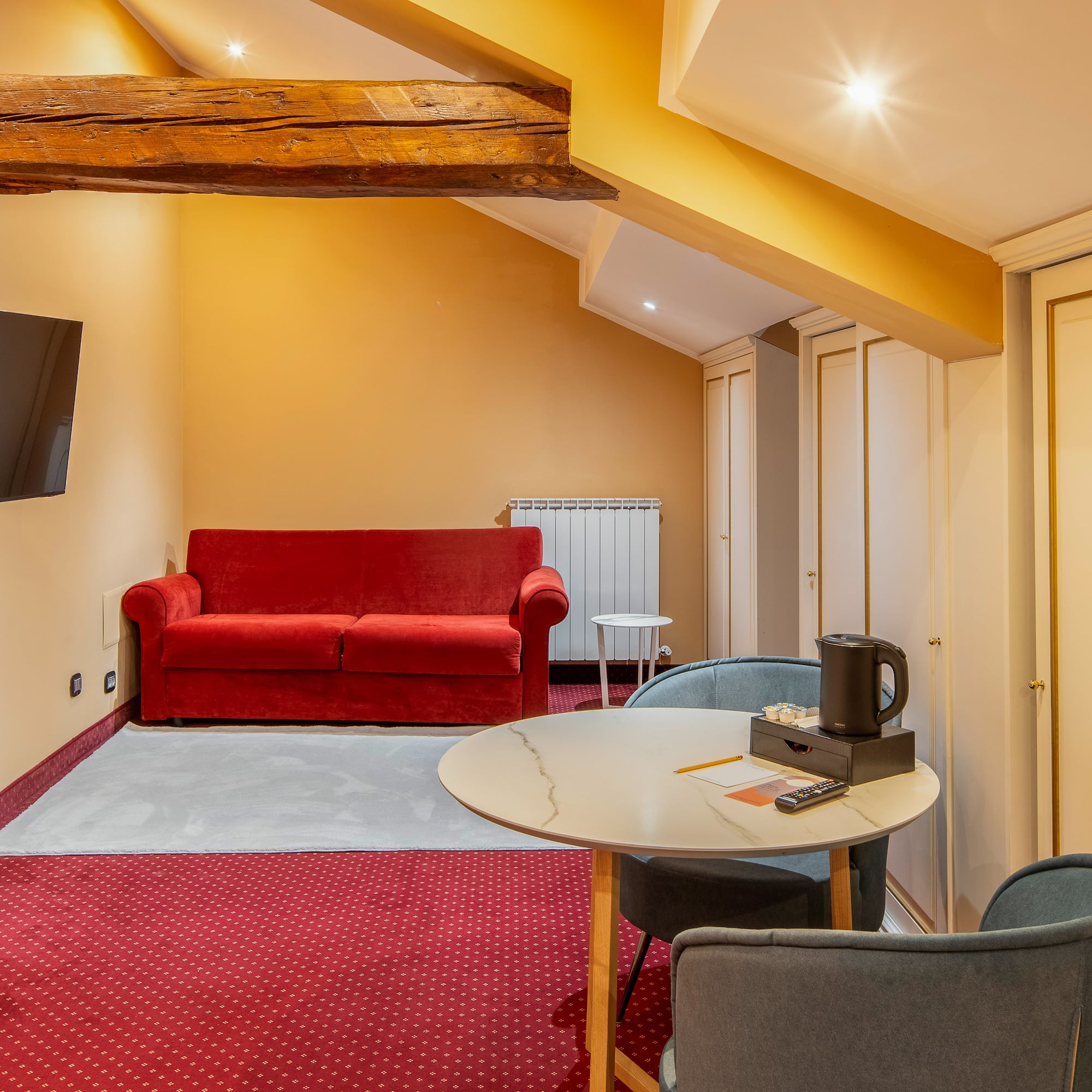 Attic hotel room with red sofa, TV, round table, and built-in wardrobes.