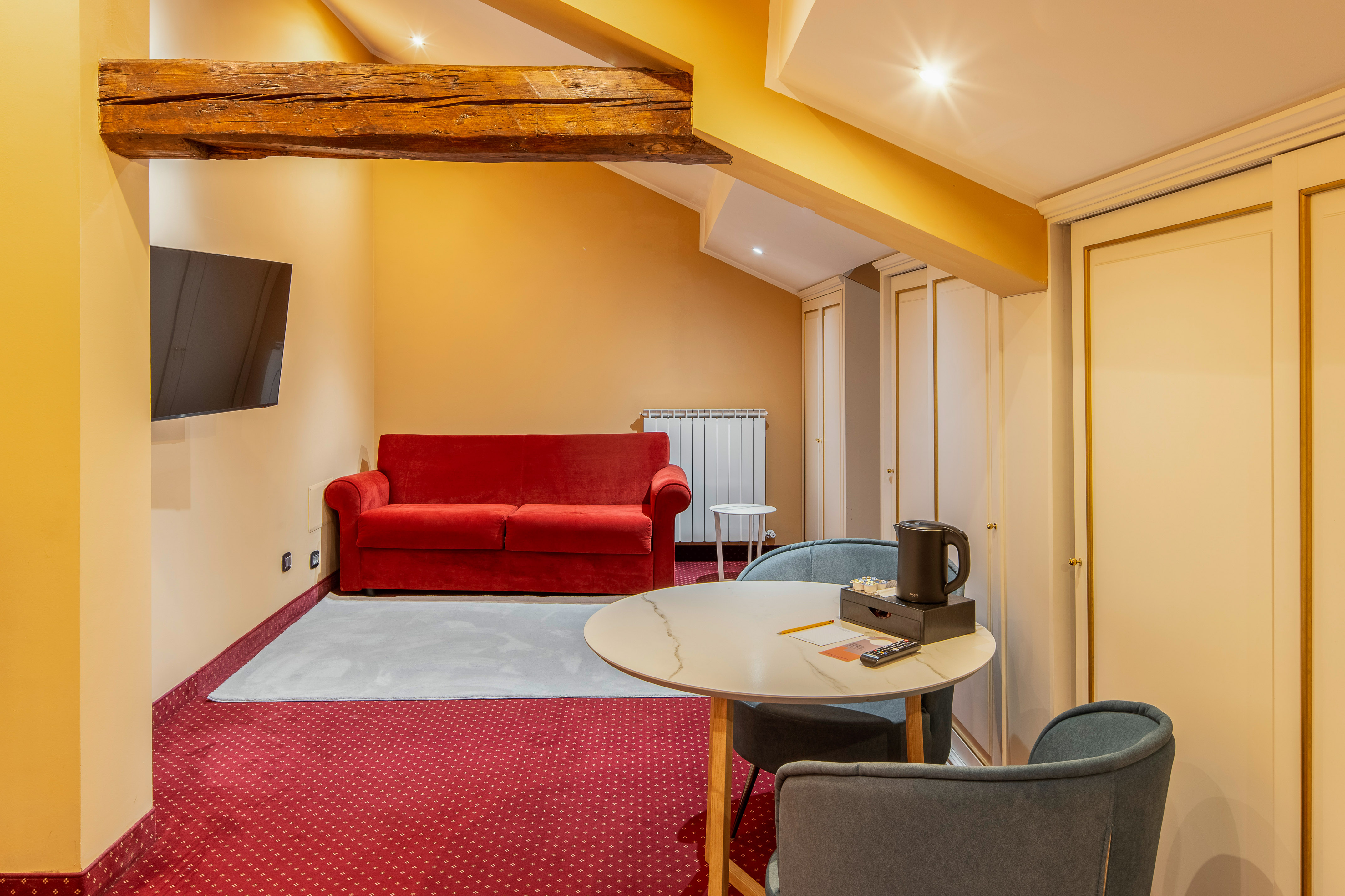 Attic hotel room with red sofa, TV, round table, and built-in wardrobes.