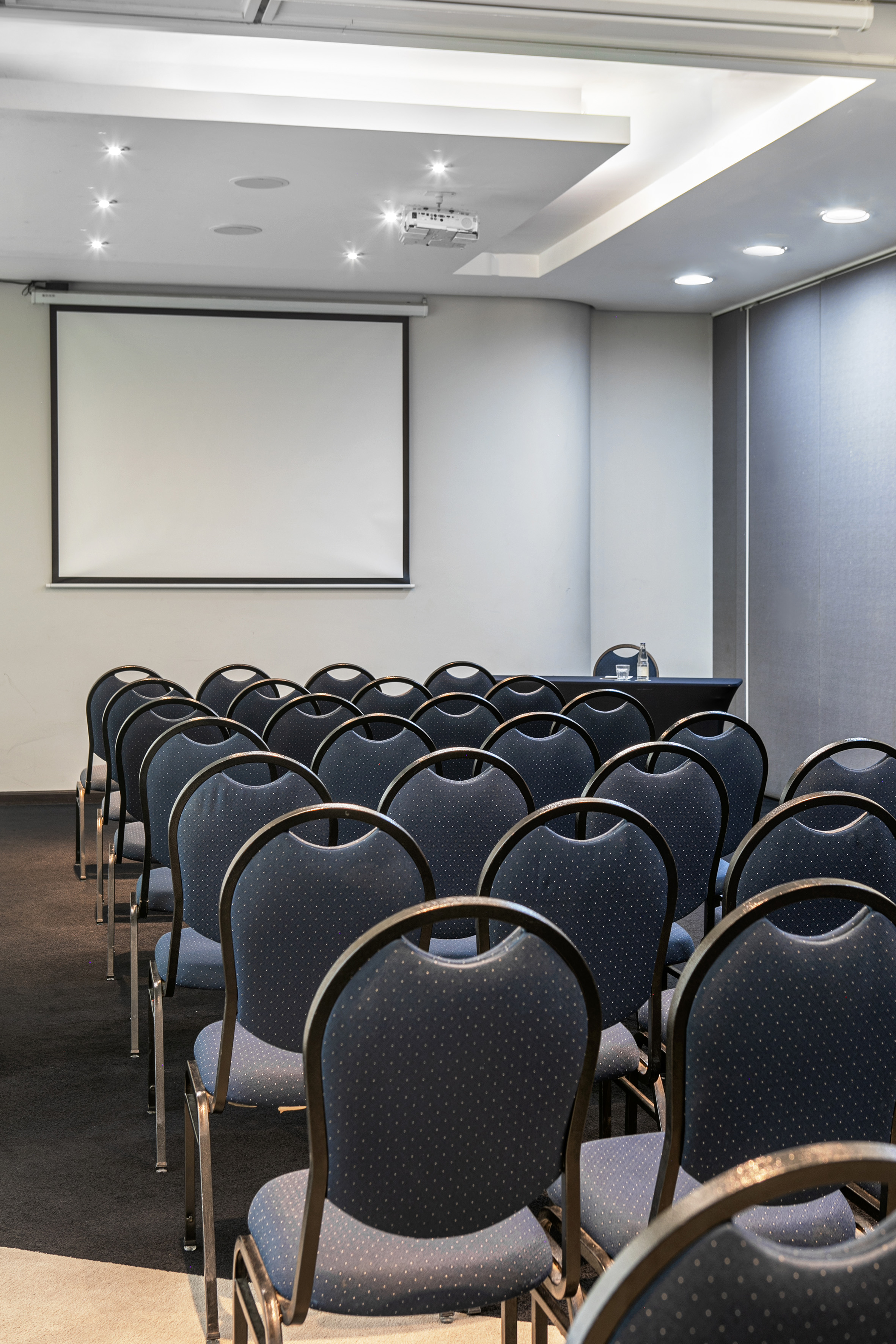 Conference room with blue chairs, projection screen, and ceiling projector.