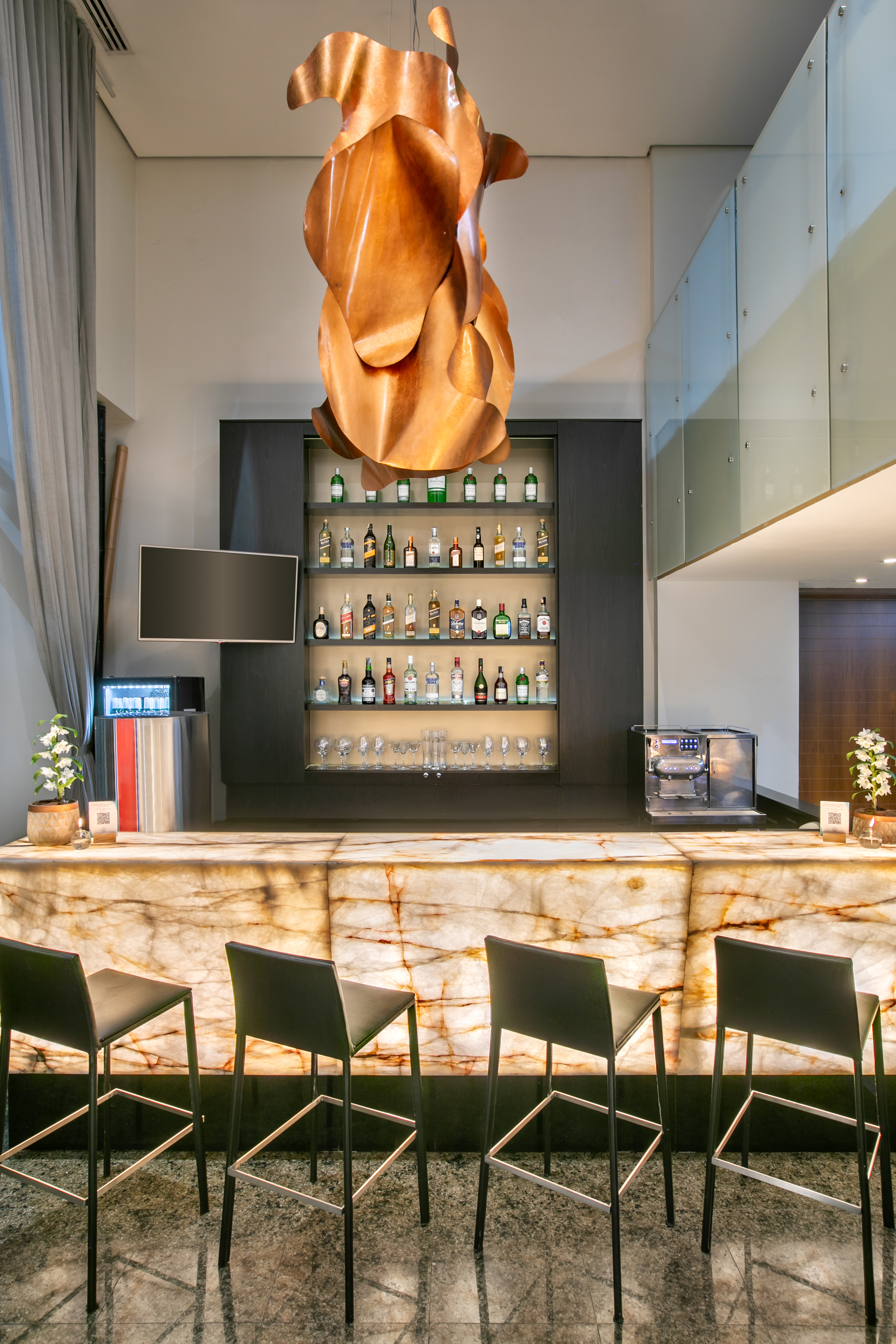 Modern bar with backlit marble counter, liquor display, and copper ceiling light.