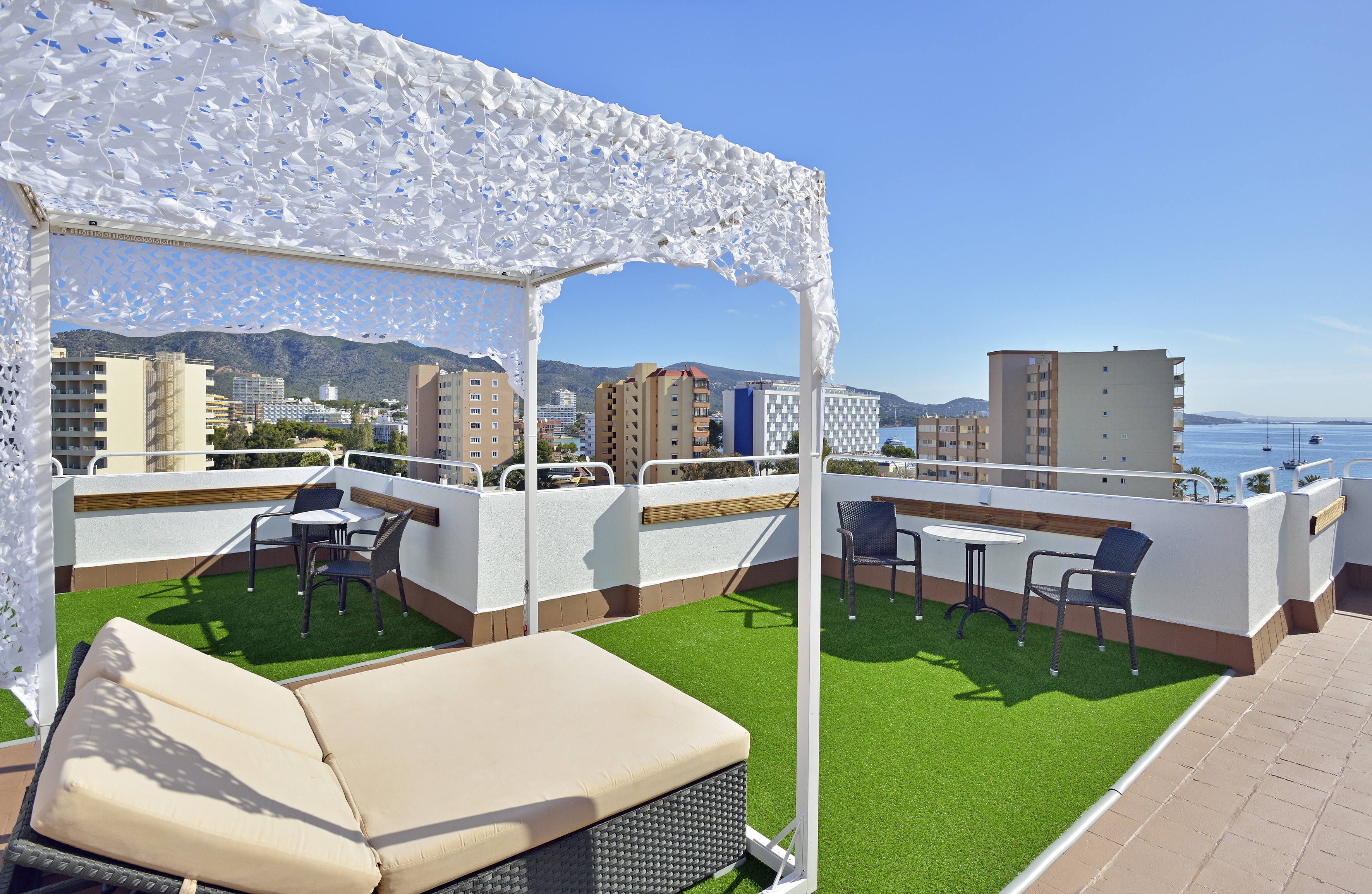 Rooftop terrace with sun canopy, daybed, green turf, and ocean view.