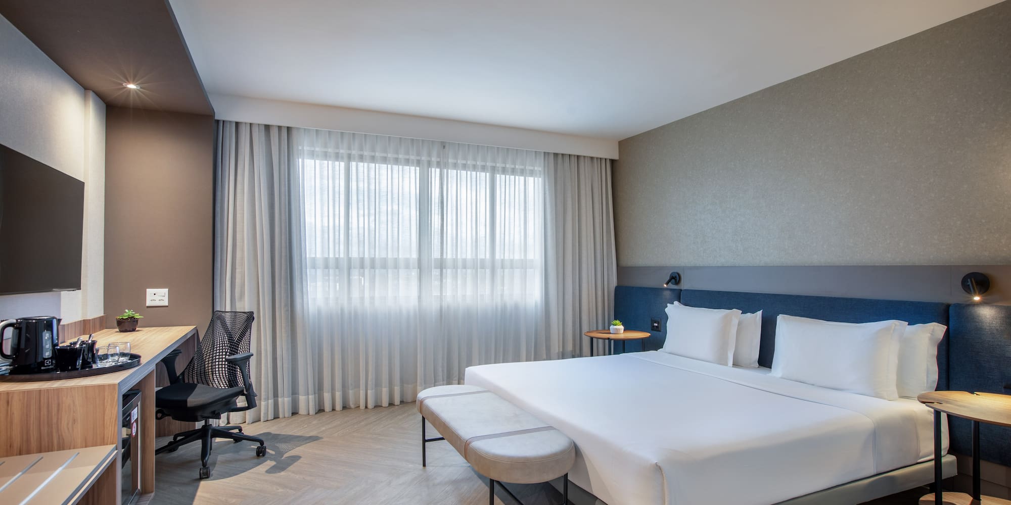 Modern hotel bedroom with king bed, work desk, and large window.