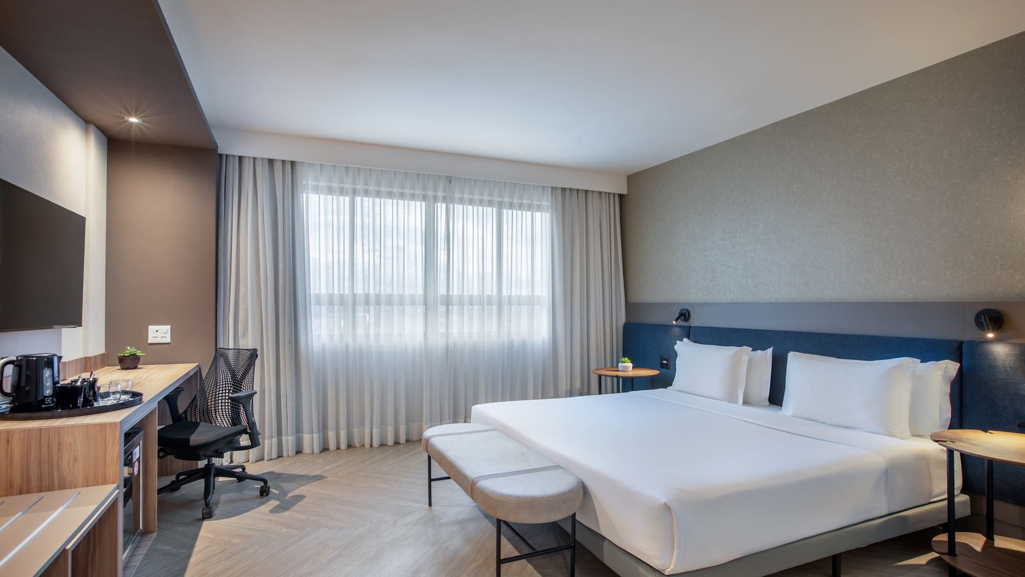 Modern hotel bedroom with king bed, work desk, and large window.