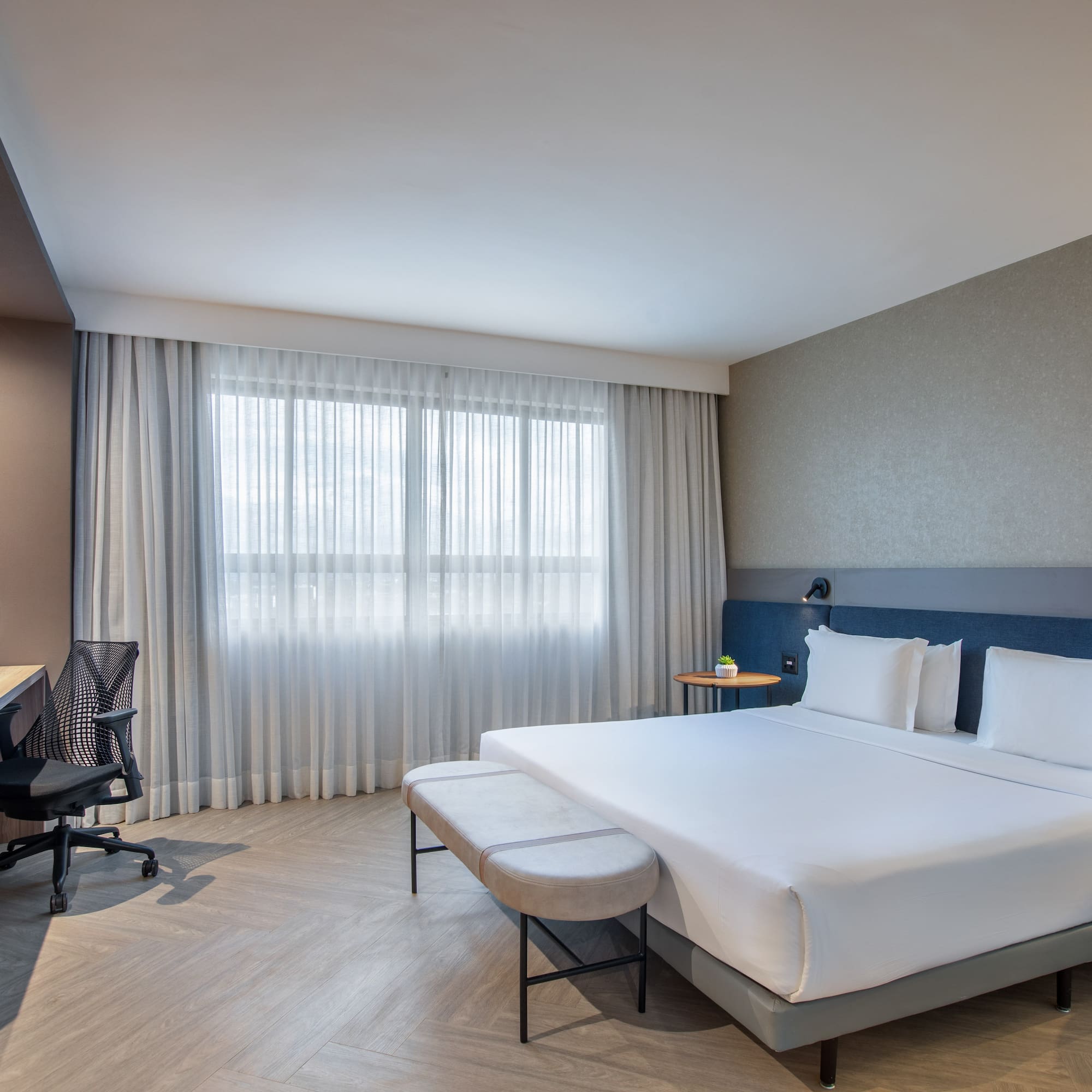 Modern hotel bedroom with king bed, work desk, and large window.